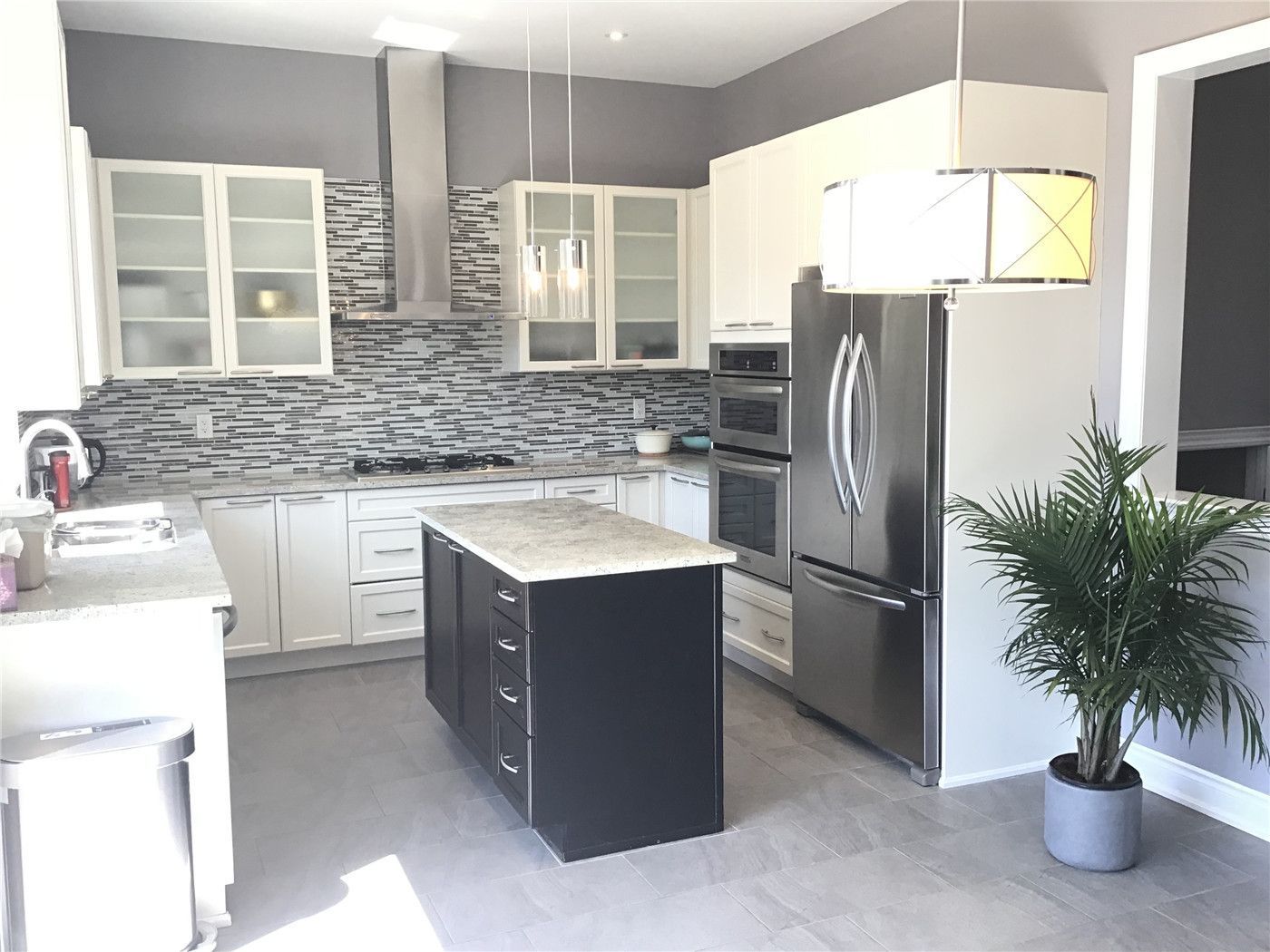 This Markham full home renovation features a bright and modern kitchen with a functional center island, stainless steel appliances, and a stylish mosaic tile backsplash. The combination of white cabinetry and dark island creates visual contrast, while the open layout enhances both workflow and space efficiency. Completed by a trusted Toronto Renovation Company, this kitchen design blends practicality with contemporary elegance.