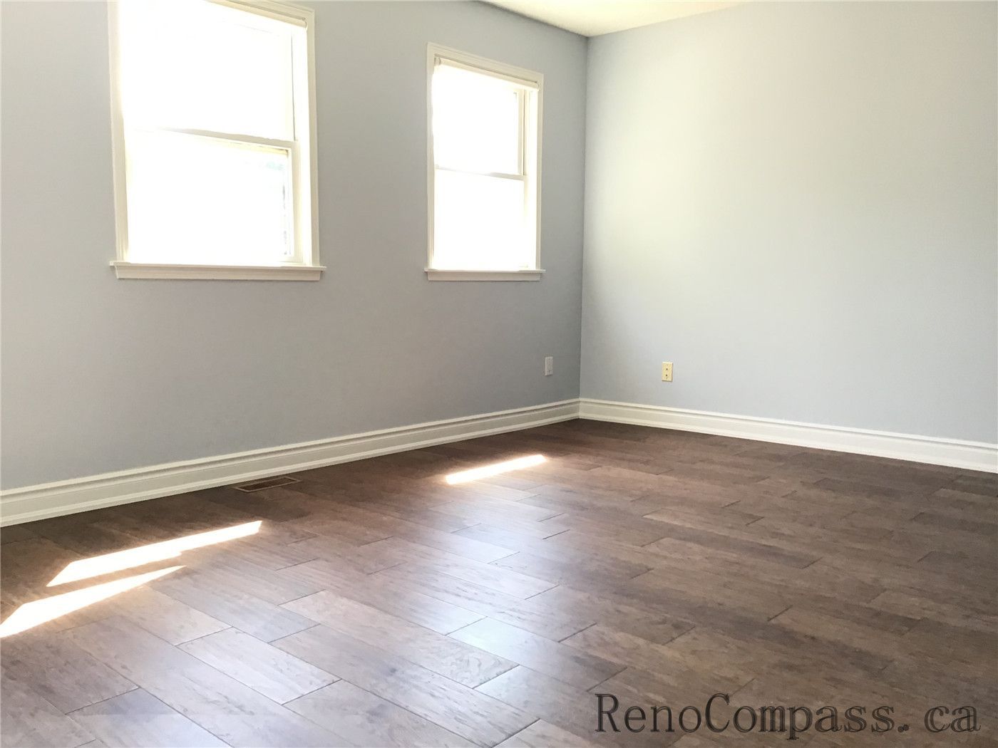 This image features a bright bedroom in a Richmond Hill renovation project, highlighting natural light from dual windows and high-quality wood flooring. The design creates an open and airy atmosphere ideal for modern living.