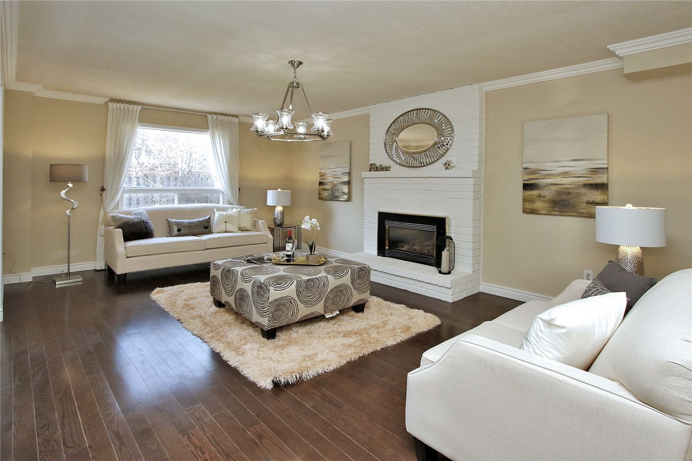 This Toronto interior design pre-sale staging features a spacious luxury living room with rich hardwood flooring, modern chandelier, and a stylish fireplace feature wall. Neutral-tone sofas, elegant décor, and soft natural lighting create a warm and sophisticated atmosphere that highlights comfort and space.