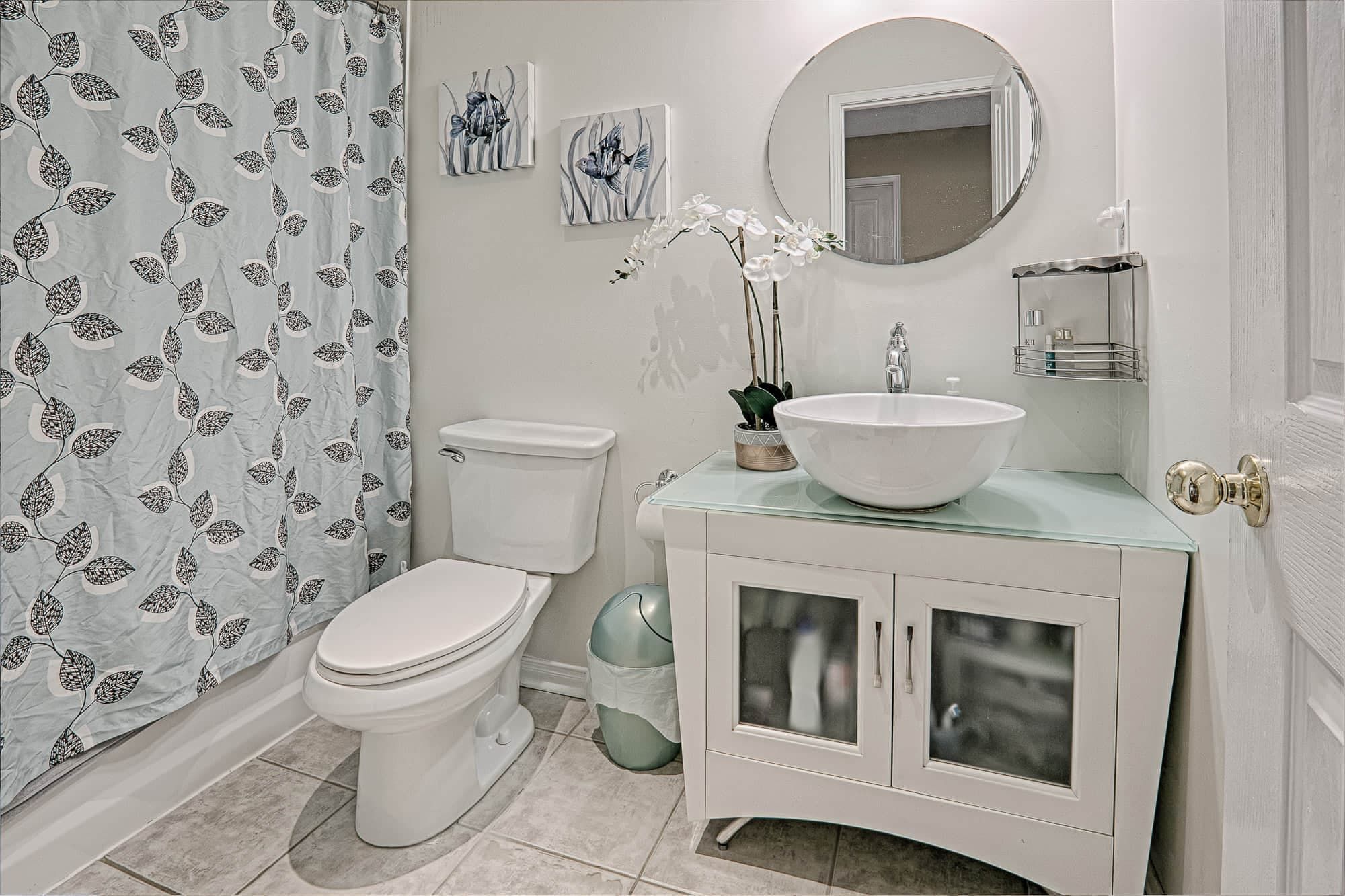This warm and minimalist bathroom interior showcases a clean and cozy home design with modern fixtures, soft neutral tones, and functional storage solutions. Featuring a round mirror vanity, vessel sink, elegant cabinetry, and subtle decorative accents, the space reflects a comfortable and welcoming lifestyle. Perfect inspiration for homeowners seeking warm minimalist interior design and practical home styling ideas in Toronto and the GTA.