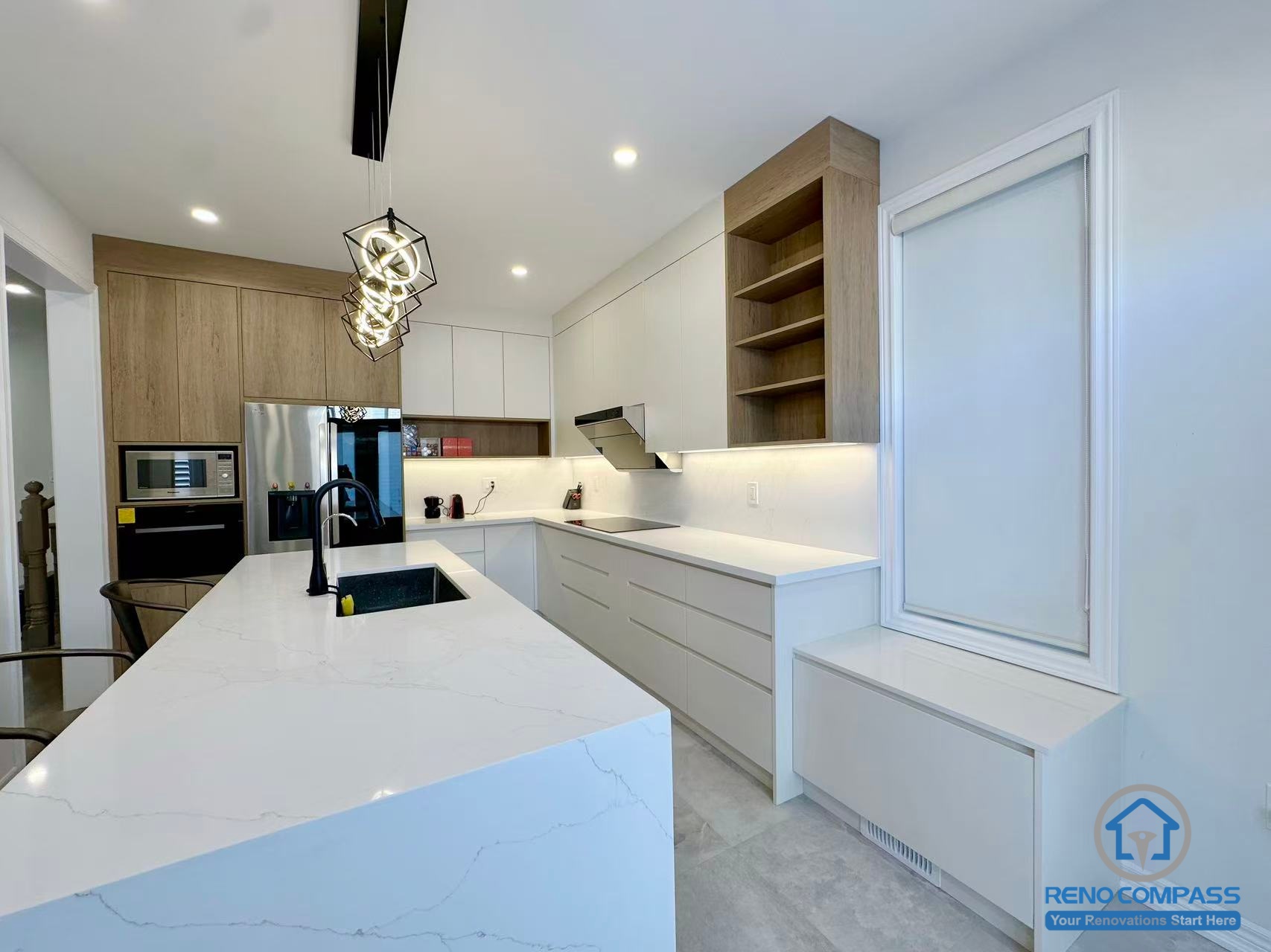 This Stouffville kitchen renovation features a long custom island with integrated sink, white quartz countertops, and a combination of wood-tone and matte white cabinetry. Recessed lighting and modern pendant fixtures enhance brightness and depth throughout the space. Designed and built by a trusted Toronto renovation company, Reno Compass Inc., this project highlights efficient workflow, clean lines, and contemporary interior craftsmanship.