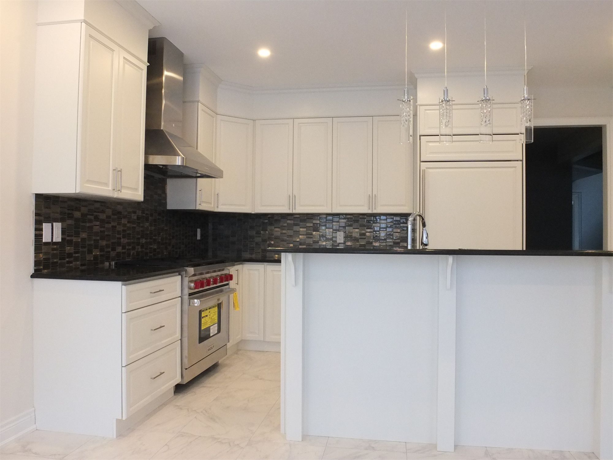 This Kleinburg interior renovation features a bright and elegant modern kitchen with custom white cabinetry, marble-style flooring, and a functional island with built-in sink. The design combines clean lines, stainless steel appliances, and a dark mosaic backsplash to create a refined contrast while maintaining a spacious and contemporary feel. The kitchen island also provides additional workspace and seating, making the space both stylish and highly practical for everyday living.