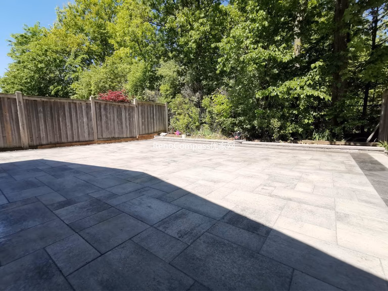 This Mississauga backyard renovation showcases a professionally installed interlocking stone patio with clean modern lines and a raised garden retaining wall. Large-format pavers create a durable and elegant outdoor flooring solution, while the stone border and planting area add depth and structure to the landscape. Completed by an experienced Toronto renovation and landscaping team, this project enhances outdoor usability, drainage, and long-term property value with low-maintenance, high-quality materials.