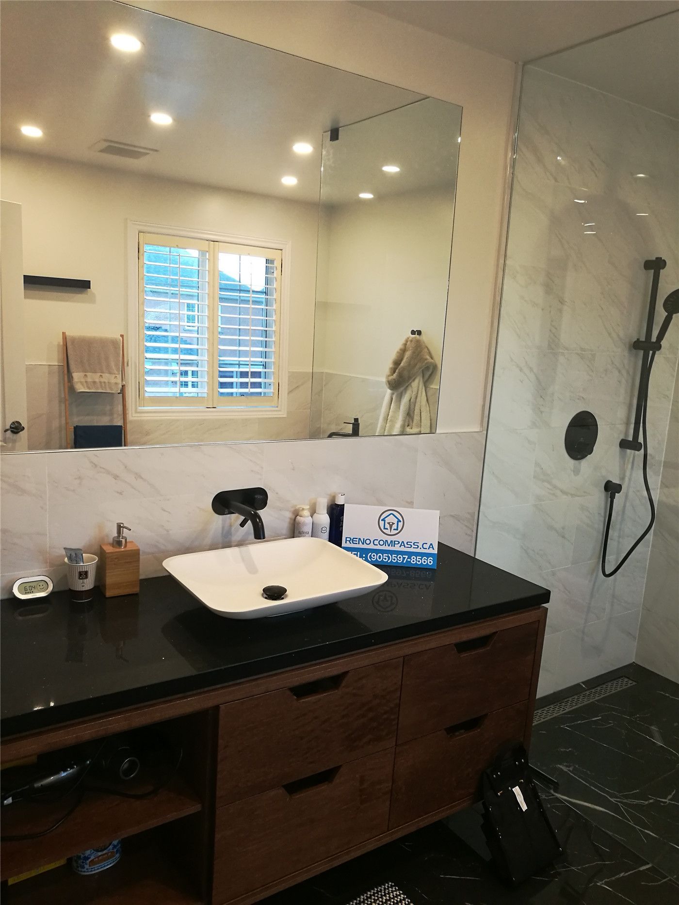 This Richmond Hill bathroom renovation features a contemporary vanity with dark wood cabinetry, a sleek vessel sink, and a large wall-to-wall mirror that enhances light and space. The design is complemented by marble-style wall finishes, black fixtures, and a modern glass shower enclosure, creating a clean and luxurious atmosphere. Completed by a professional Toronto renovation company, this project highlights high-quality materials, practical storage solutions, and timeless modern design for everyday comfort.