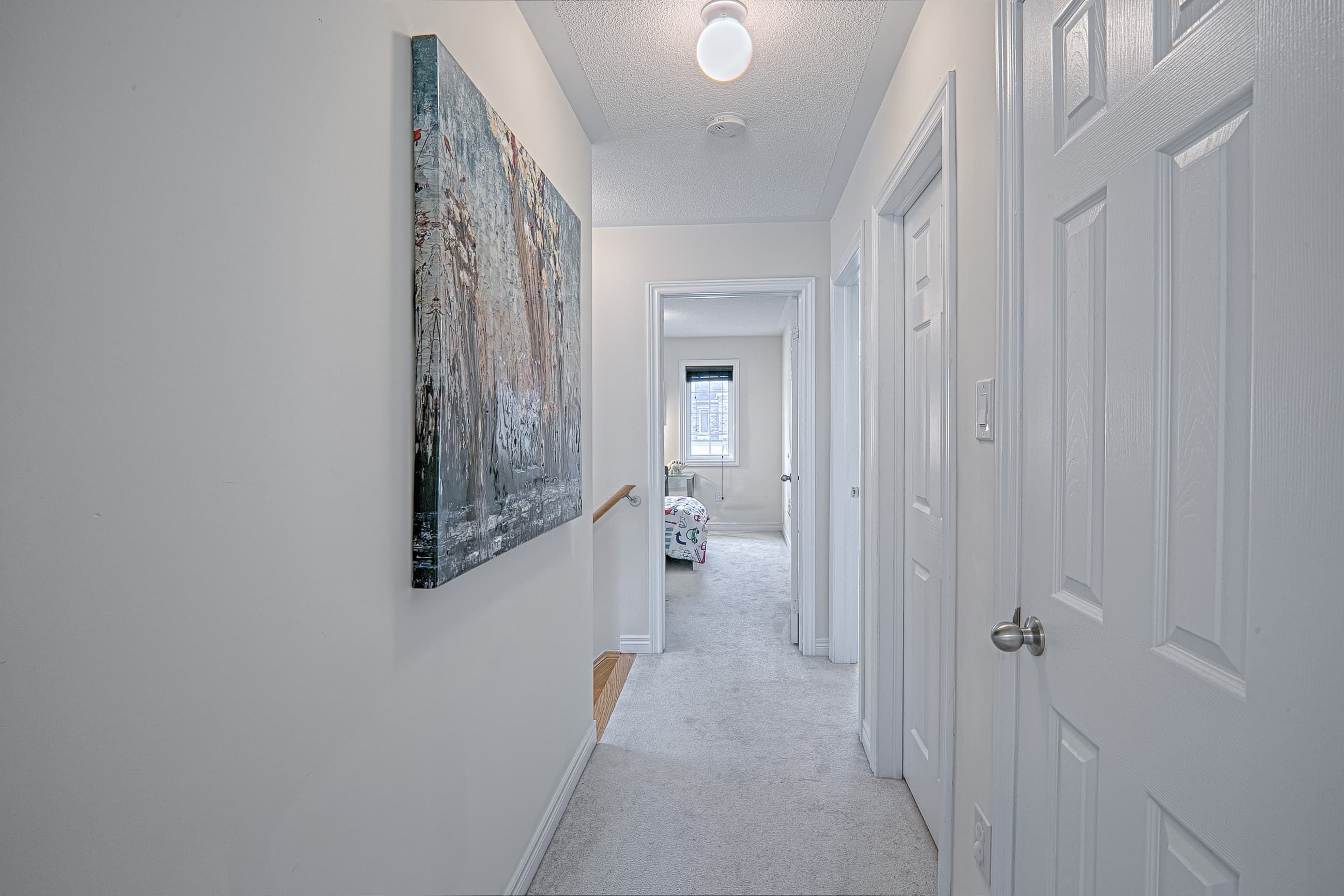 This modern hallway renovation features a clean neutral palette, soft carpeting, and bright overhead lighting that enhances the sense of openness throughout the upper floor. The streamlined layout connects bedrooms and living spaces seamlessly, while contemporary wall art adds visual interest and warmth. Designed to improve flow, comfort, and everyday functionality, this interior upgrade reflects the high-quality craftsmanship of a trusted Toronto renovation company specializing in full home renovation and modern residential interiors.
