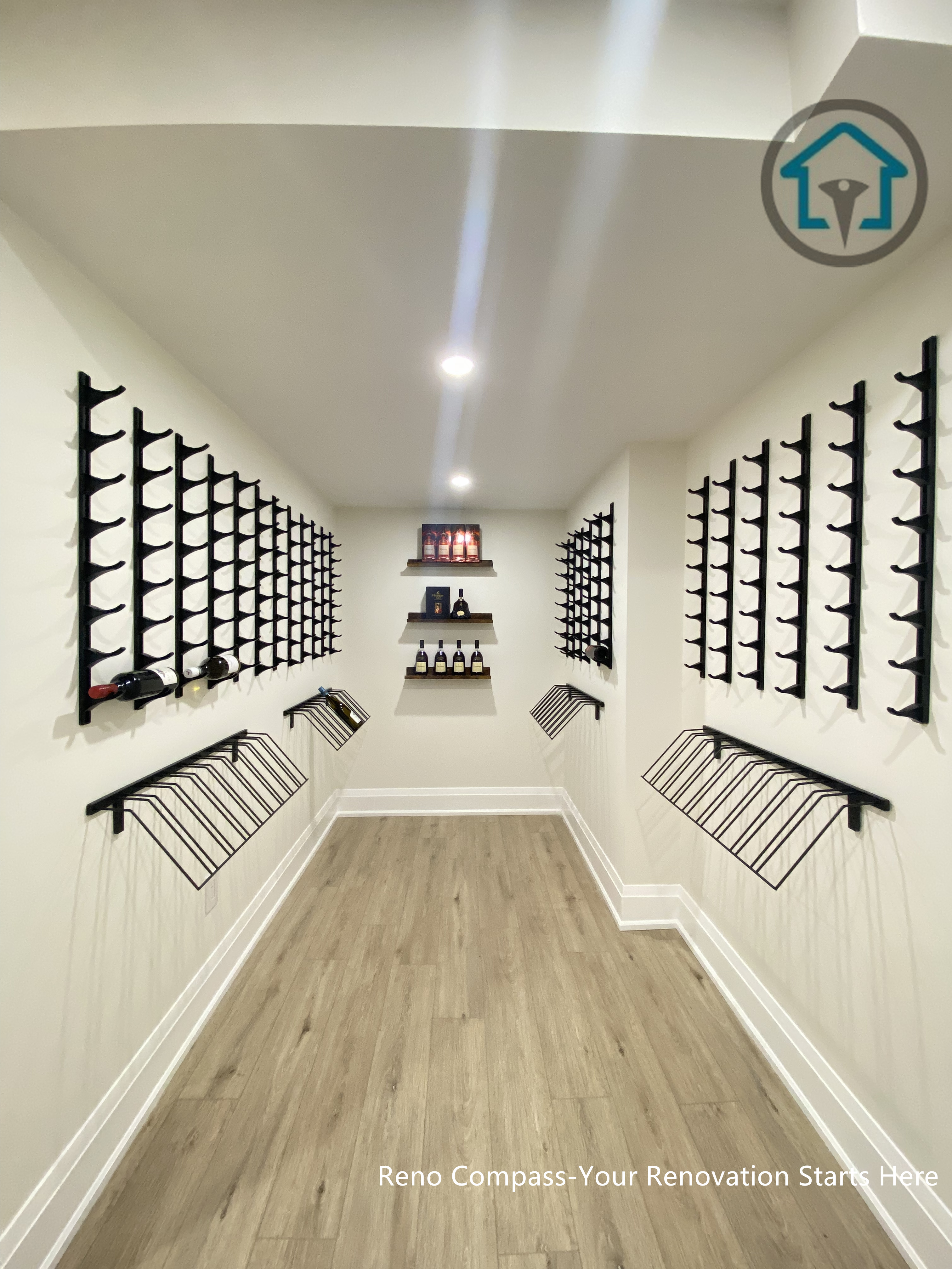 This image features a custom-designed wine cellar within a Richmond Hill interior renovation, showcasing symmetrical wall-mounted wine racks and a clean, gallery-style layout. The narrow corridor design maximizes bottle storage while maintaining visual order and ease of access. Neutral finishes and wood flooring add warmth and balance to the space. Designed and completed by Reno Compass, this wine storage solution reflects a refined approach to functional interior design for homes in Richmond Hill.