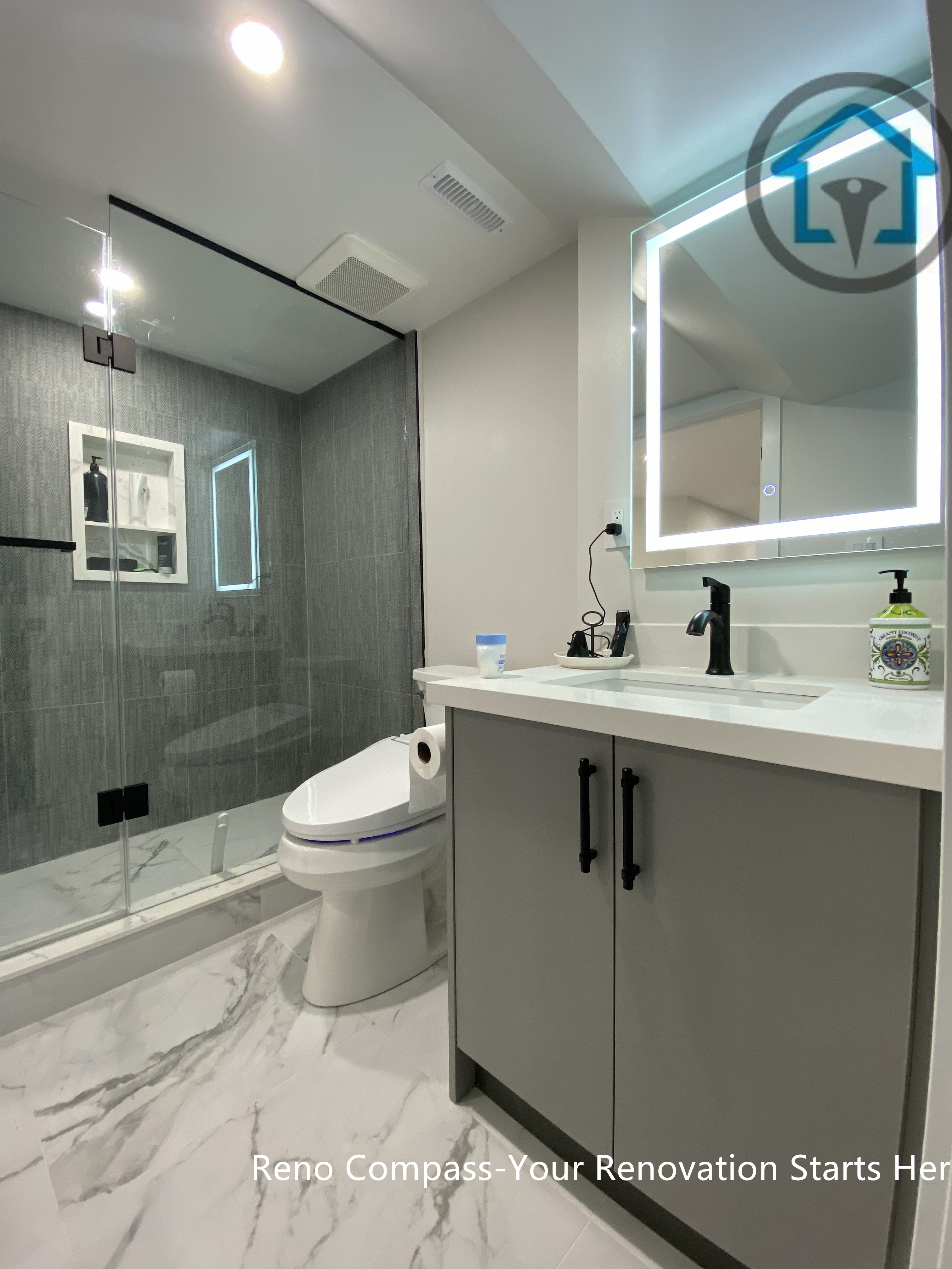This Stouffville basement bathroom renovation highlights a frameless glass shower, large-format wall tiles, marble-look flooring, LED mirror, and modern vanity with matte black fixtures. The layout maximizes space efficiency while maintaining a clean, contemporary aesthetic, completed by Reno Compass Inc.