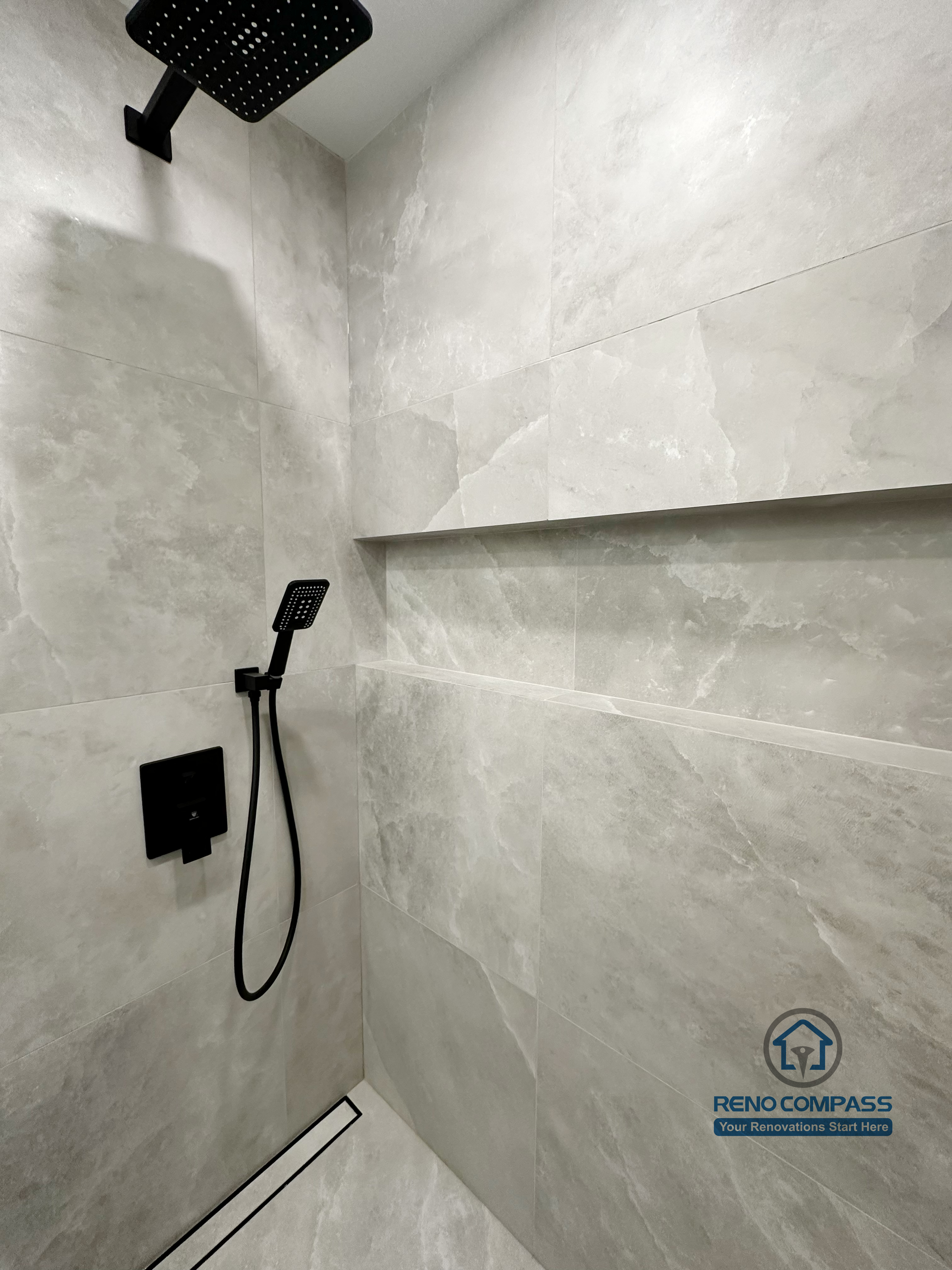 Bathroom renovation in Markham featuring a walk-in shower with large-format tile walls, a built-in shower niche, linear floor drain, and matte black rain shower fixtures. The design delivers a clean, modern look with a focus on durability and easy maintenance.
