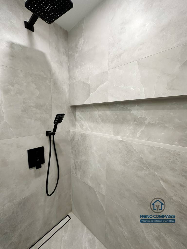 Bathroom renovation in Markham featuring a walk-in shower with large-format tile walls, a built-in shower niche, linear floor drain, and matte black rain shower fixtures. The design delivers a clean, modern look with a focus on durability and easy maintenance.