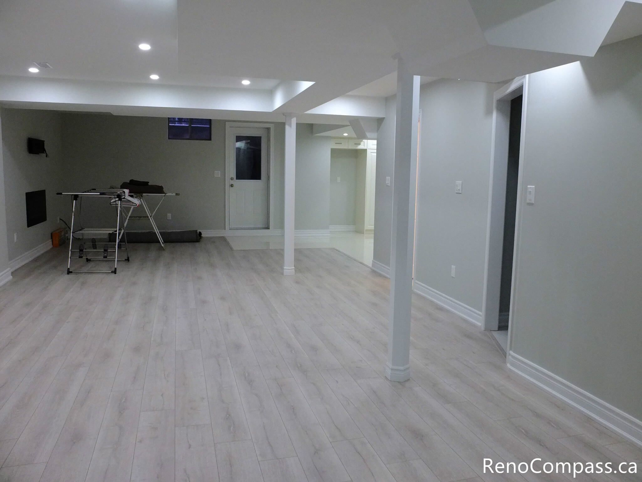 This Markham basement renovation showcases a spacious open-concept layout with light wood-look vinyl flooring, recessed pot lights, and clean modern finishes. Structural support columns are seamlessly integrated into the design, creating a bright and functional living area ideal for entertainment, home office, or rental use. Completed by a professional Toronto Renovation Company, Reno Compass Inc.
