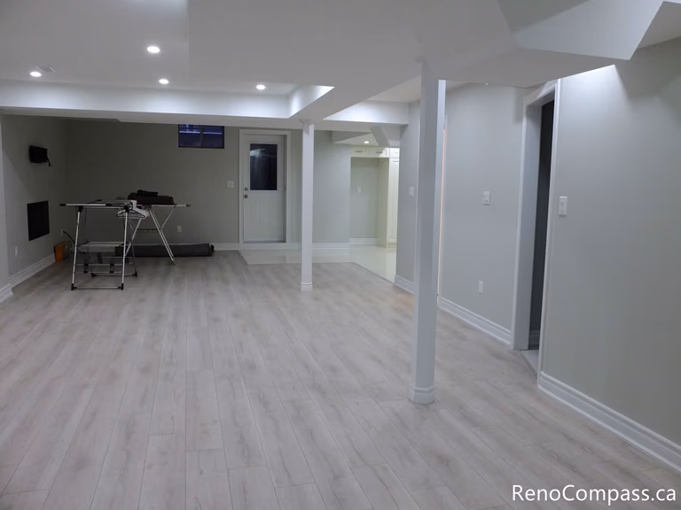 This Markham basement renovation showcases a spacious open-concept layout with light wood-look vinyl flooring, recessed pot lights, and clean modern finishes. Structural support columns are seamlessly integrated into the design, creating a bright and functional living area ideal for entertainment, home office, or rental use. Completed by a professional Toronto Renovation Company, Reno Compass Inc.