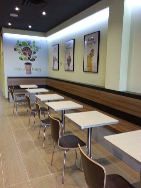 Commercial bubble tea shop renovation in Toronto featuring a modern dining area with wall bench seating, minimalist tables and chairs, decorative drink posters, and warm lighting design. The renovated space creates a comfortable and stylish environment for customers to enjoy their drinks while maintaining efficient space planning for a busy bubble tea store. Completed by a professional Toronto renovation company.