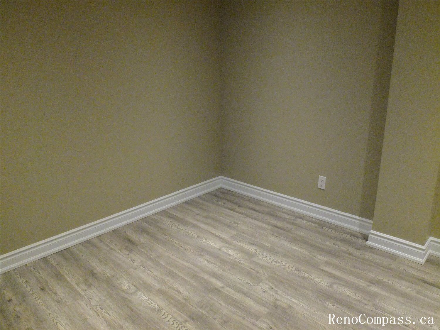 This image highlights a clean finished corner of the Ajax basement renovation featuring modern vinyl plank flooring, freshly painted walls, and decorative white baseboard trim. The neutral color palette and durable flooring create a practical and comfortable basement living space suitable for a family room, home office, or recreation area. Completed by a professional Toronto Renovation Company, the renovation emphasizes clean finishes, functional design, and long-lasting materials.