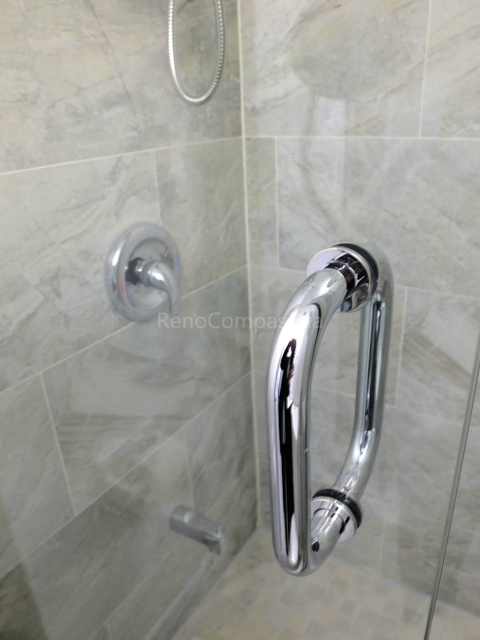 This image features a close-up detail of a frameless glass shower door handle installed during a North York interior renovation project. The polished chrome handle is paired with marble-look wall tiles and a minimalist shower control layout, highlighting durability, safety, and modern bathroom design. The clean installation reflects careful material selection and precise workmanship by a trusted Toronto renovation company.