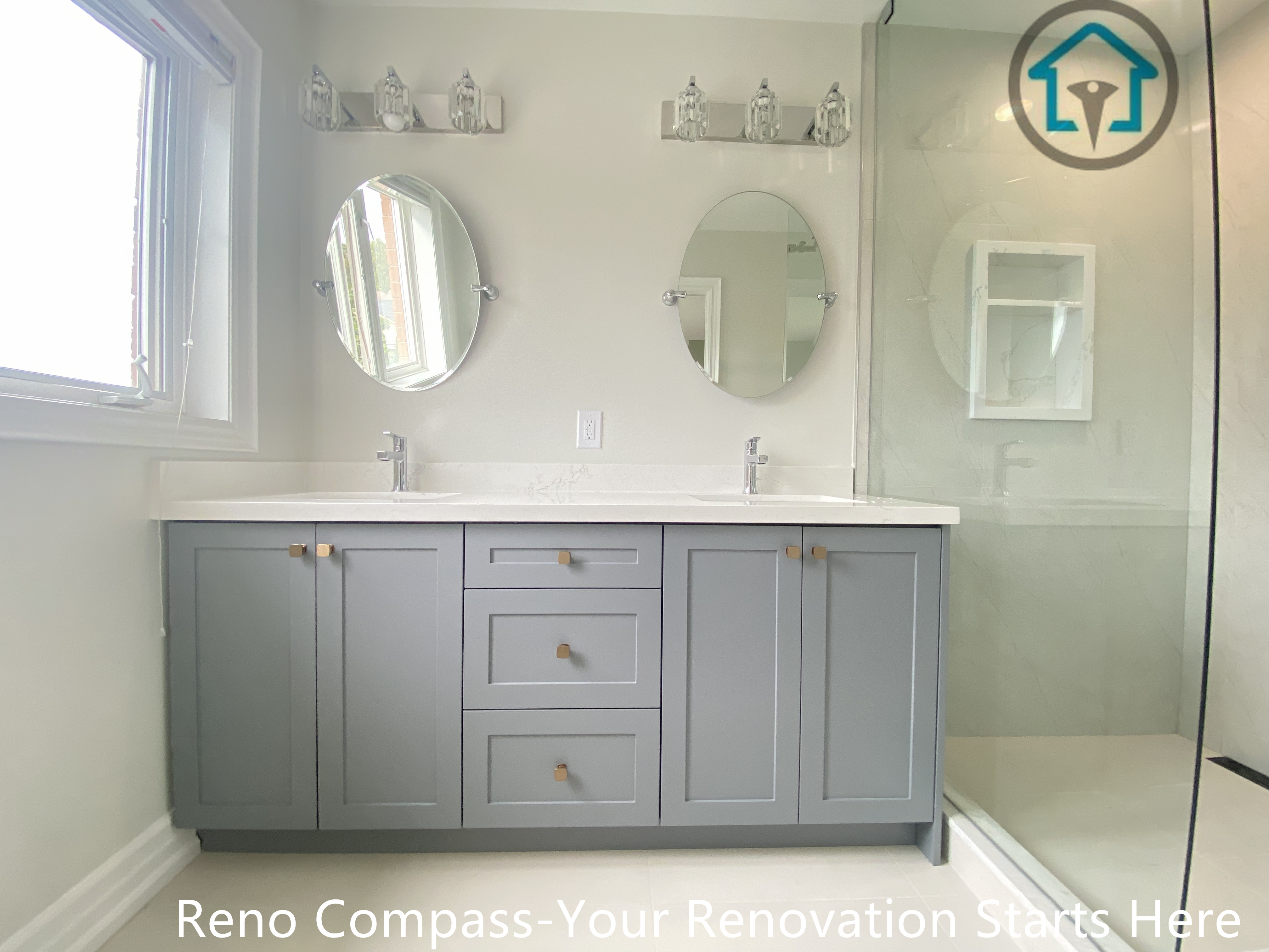 This bathroom renovation features a clean and modern design centered around a custom double vanity and a frameless glass shower. The grey vanity cabinetry provides generous storage while maintaining a soft, contemporary look, paired with a white quartz countertop for durability and easy maintenance. Dual round mirrors and minimalist lighting fixtures enhance symmetry and brightness, creating a balanced and functional vanity area.