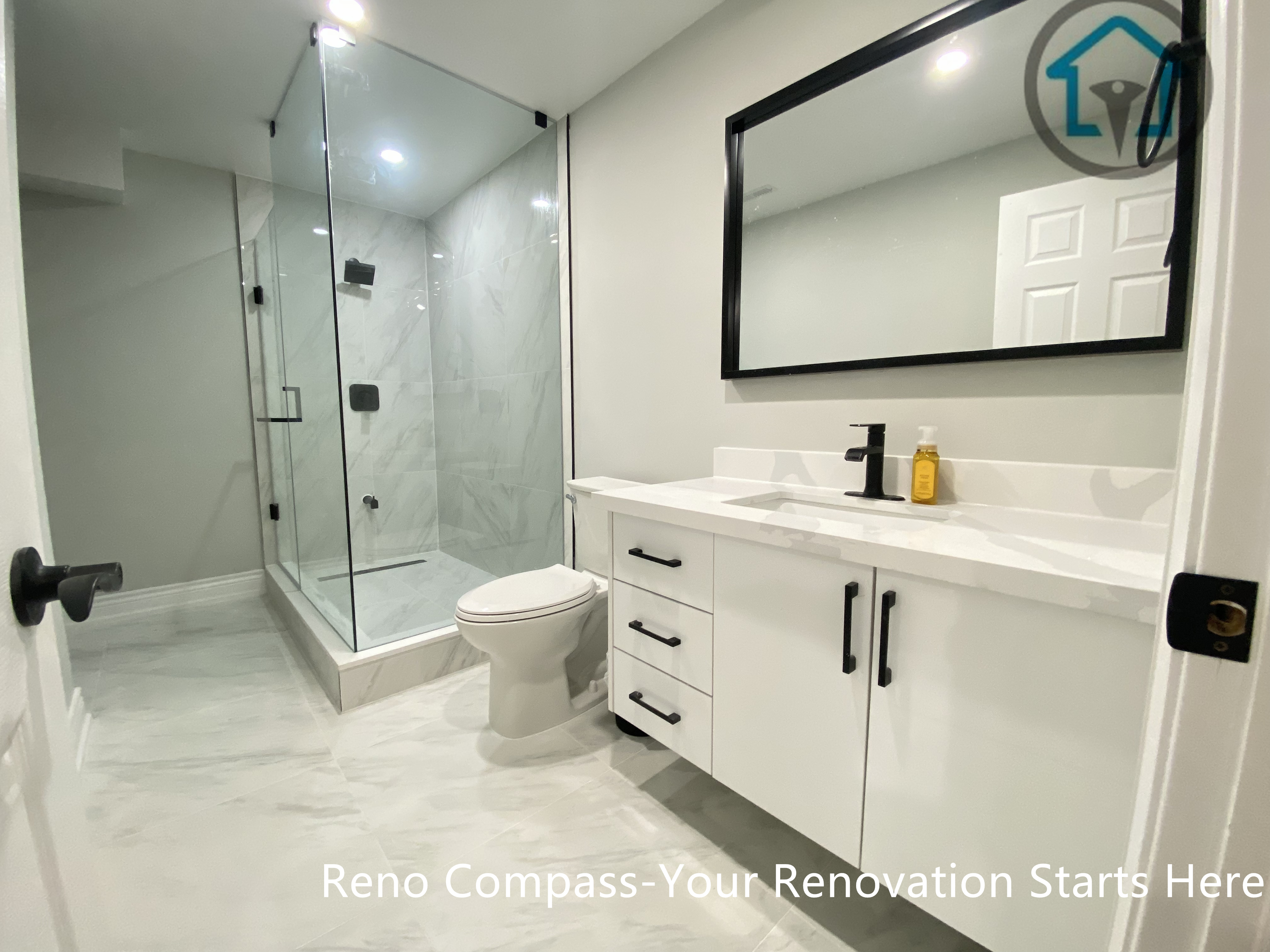 A modern basement bathroom renovation in Stouffville featuring a glass-enclosed shower, large-format tile finishes, a clean white vanity with black hardware, and recessed lighting for a bright, functional layout.