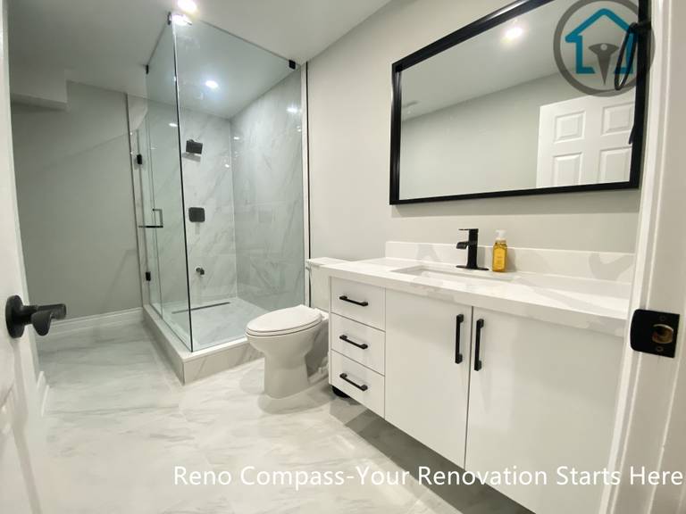 A modern basement bathroom renovation in Stouffville featuring a glass-enclosed shower, large-format tile finishes, a clean white vanity with black hardware, and recessed lighting for a bright, functional layout.