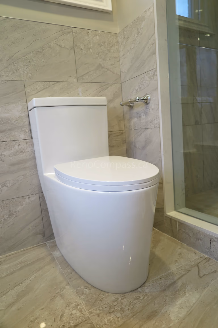 This Markham bathroom renovation features a sleek modern one-piece toilet paired with marble-style wall and floor tiles for a clean and contemporary look. The space includes glass shower enclosure detailing and high-quality tile installation that enhances durability and easy maintenance. Completed by Reno Compass, a professional renovation contractor specializing in bathroom renovations, tile installation, and full interior remodeling across Markham and the Greater Toronto Area.