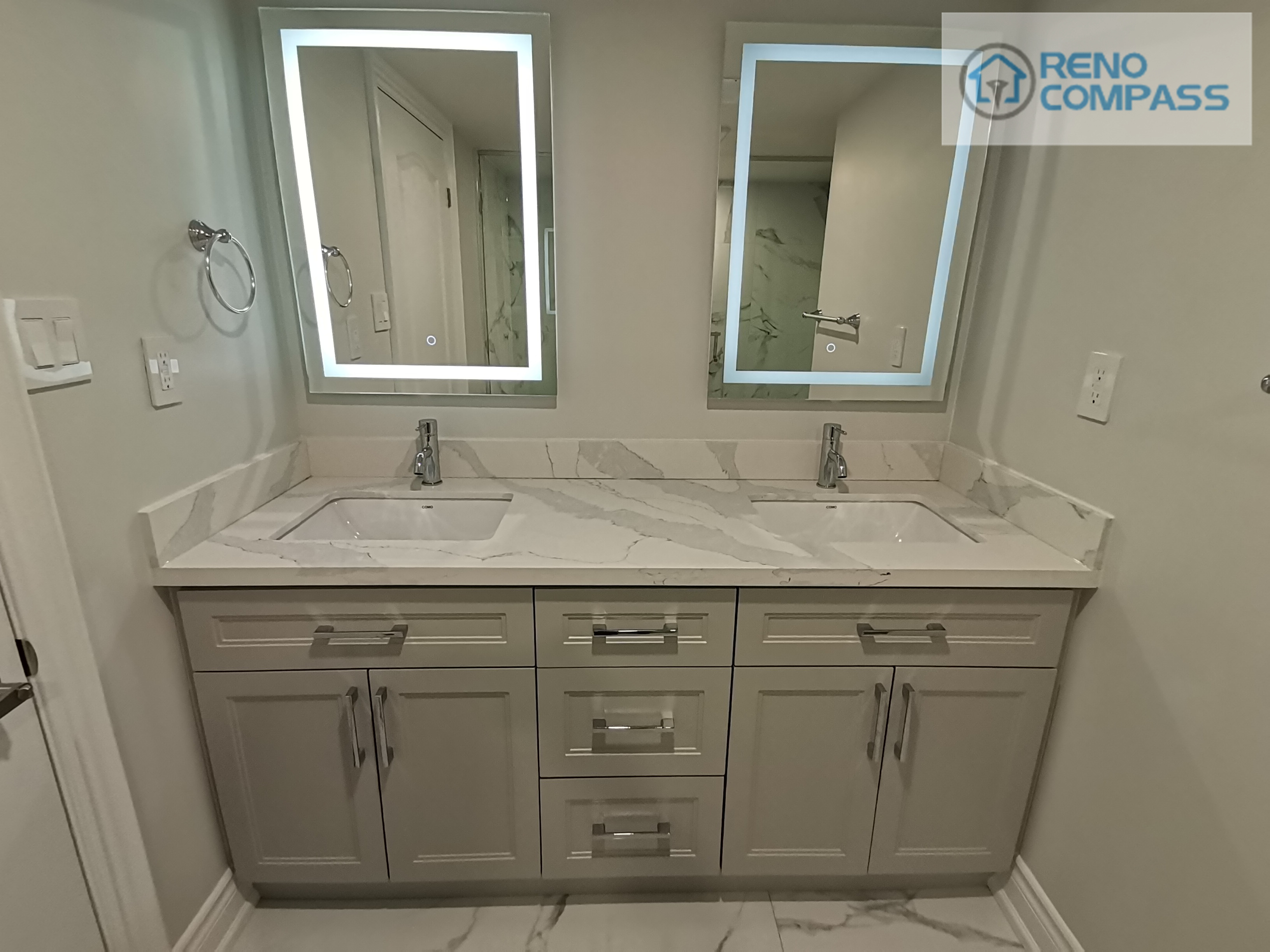 This Woodbridge basement bathroom renovation features a clean and functional double vanity layout designed for everyday comfort and efficiency. The custom grey vanity provides ample storage, paired with a seamless quartz countertop and dual undermount sinks. Backlit LED mirrors enhance lighting quality while maintaining a modern, minimal aesthetic. Neutral wall tones and coordinated finishes help the space feel bright, balanced, and well-proportioned—ideal for a basement bathroom intended for regular family use or guest accommodation.
