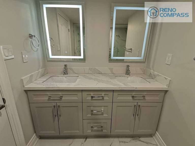 This Woodbridge basement bathroom renovation features a clean and functional double vanity layout designed for everyday comfort and efficiency. The custom grey vanity provides ample storage, paired with a seamless quartz countertop and dual undermount sinks. Backlit LED mirrors enhance lighting quality while maintaining a modern, minimal aesthetic. Neutral wall tones and coordinated finishes help the space feel bright, balanced, and well-proportioned—ideal for a basement bathroom intended for regular family use or guest accommodation.