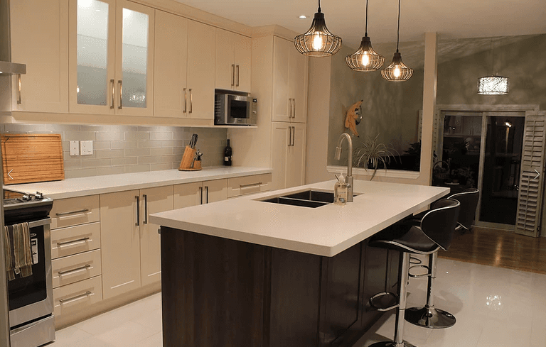 This Mississauga kitchen renovation features custom cream cabinetry, a large quartz island, modern pendant lighting, and upgraded backsplash design. Completed by a professional Toronto renovation company, the project focuses on improving functionality, storage, and modern aesthetics. The spacious island with built-in sink and seating enhances daily use and entertaining, while new lighting and finishes create a warm, elegant atmosphere. Ideal for homeowners in Mississauga seeking a stylish and practical kitchen upgrade with high-quality craftsmanship and thoughtful layout planning.