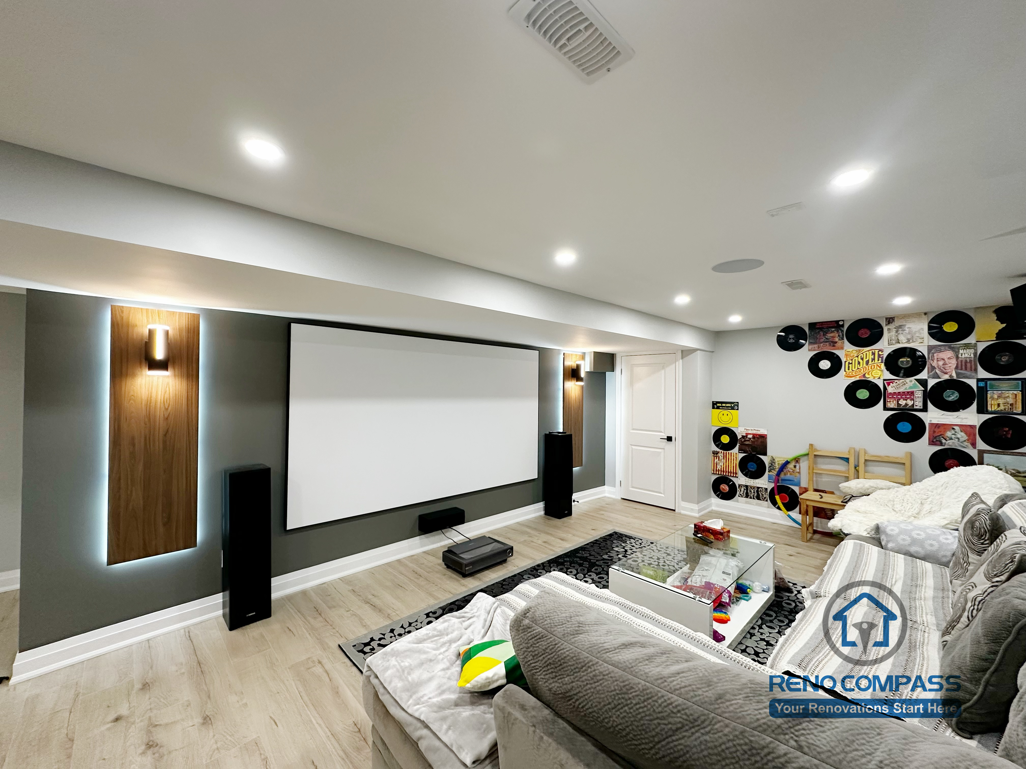 This modern Newmarket basement renovation features a custom home theater setup with a built-in projector screen, recessed ceiling lighting, and a clean, contemporary layout. The finished basement combines entertainment and family living, showcasing professional lighting design, smooth ceiling work, and warm flooring for a comfortable and functional space.