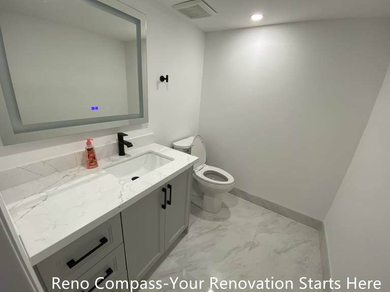 This basement bathroom renovation in Bradford features a clean, modern design focused on durability and everyday functionality. The space is finished with large-format marble-look floor tiles that visually expand the room while improving moisture resistance and ease of maintenance. A custom vanity with flat-panel cabinetry provides practical storage, paired with a quartz countertop and an undermount sink for a seamless, low-maintenance surface. Matte black fixtures and hardware add contrast and definition, creating a balanced and contemporary basement bathroom suitable for guest use or rental living. Designed and built as part of a complete Bradford basement renovation by Reno Compass Inc., this bathroom reflects careful planning, precise detailing, and long-term usability.