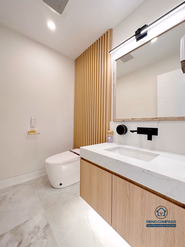 Contemporary bathroom renovation in Toronto featuring a custom wood-grain vanity, integrated sink, modern wall-mounted faucet, vertical wood slat accent wall, and soft neutral finishes. Completed by a professional Toronto renovation company with a focus on warm minimalism and refined detailing.