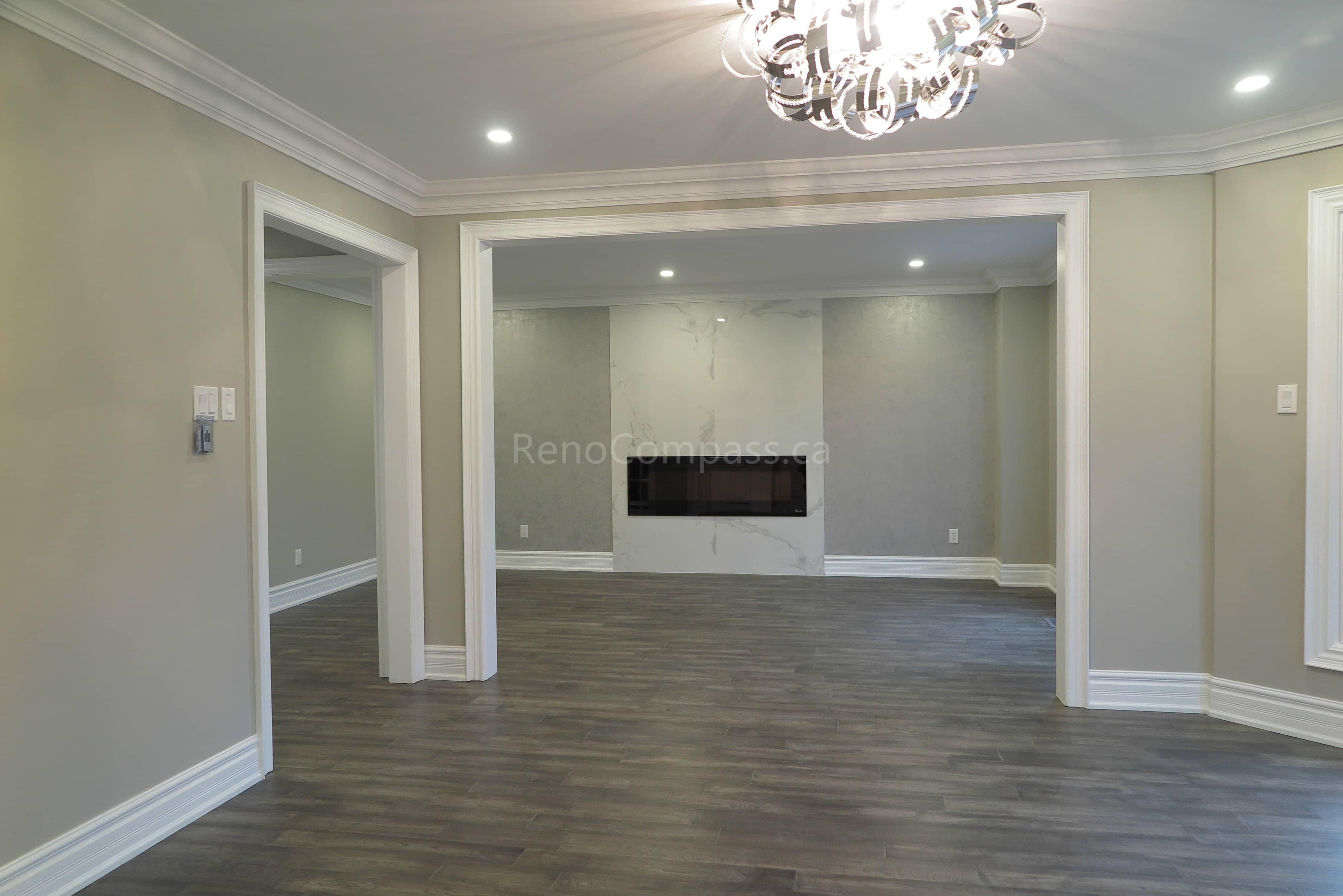 This Markham interior renovation highlights a modern living room upgrade featuring a sleek built-in linear fireplace and a marble-style feature wall. The space is finished with warm neutral paint tones, crown molding details, and newly installed dark hardwood flooring, creating a clean and elegant contemporary atmosphere. Completed by Reno Compass, a trusted renovation contractor providing professional interior renovation and custom finishing services in Markham and the Greater Toronto Area.