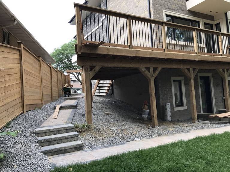 This Markham landscaping renovation features a raised wooden deck, interlocking stone walkway, decorative gravel drainage, and a natural wood privacy fence. The design improves backyard accessibility while creating a clean and functional outdoor space beneath and around the deck area. Completed by a trusted Toronto Renovation Company, the project combines durable materials with thoughtful landscaping to enhance both usability and overall outdoor aesthetics.