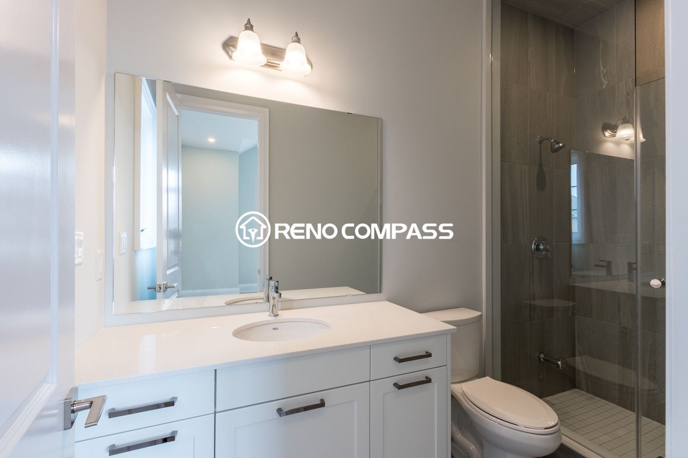 Contemporary bathroom renovation in Newmarket featuring a modern vanity with quartz countertop, large wall mirror, and a frameless glass shower enclosure. Completed by a professional Toronto renovation company, this design creates a bright and practical bathroom space with a clean modern style.