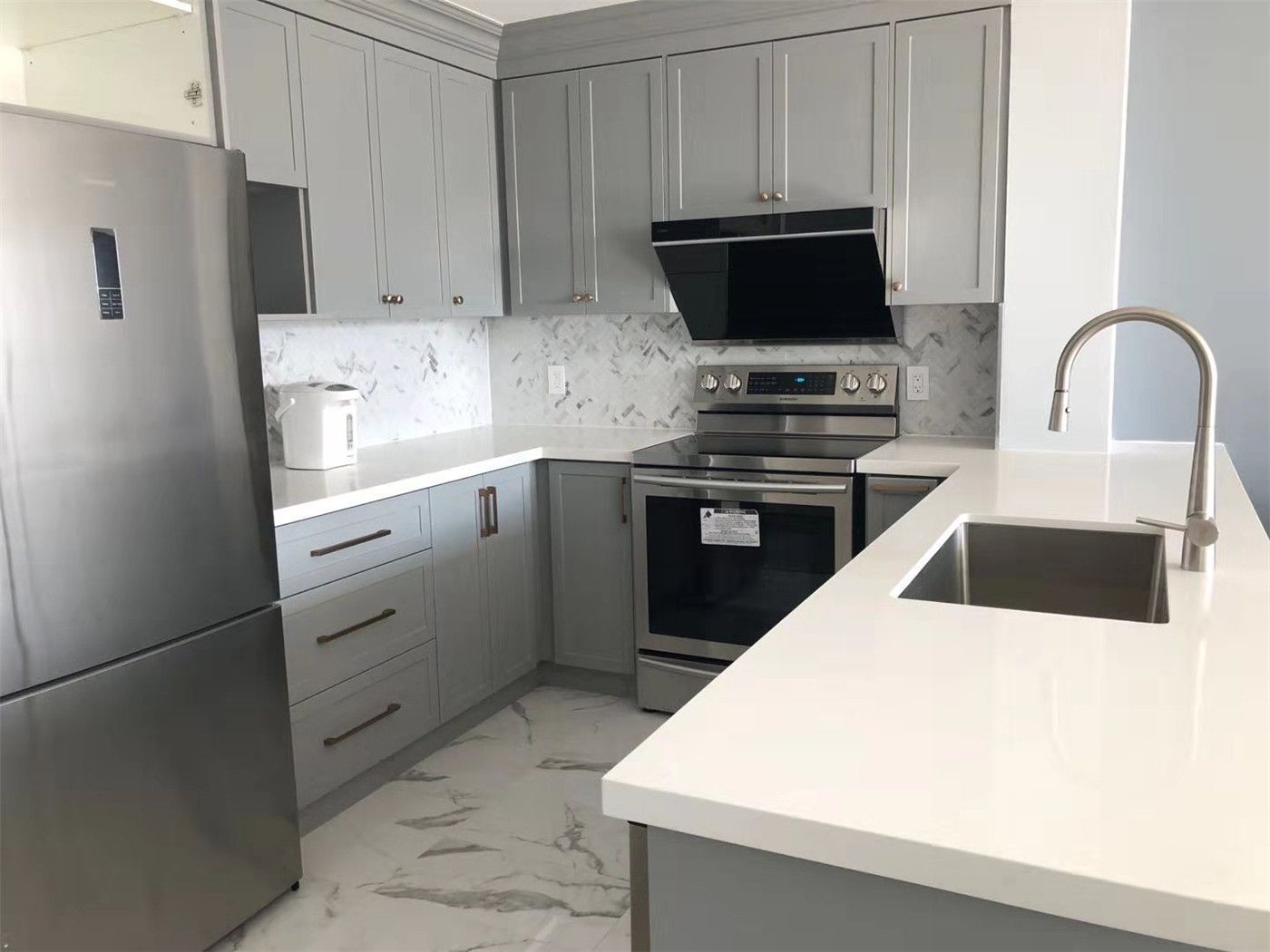 Modern condo kitchen renovation in Richmond Hill featuring sleek grey shaker cabinets, white quartz countertops, and stainless steel appliances. The design includes a functional kitchen island with an integrated sink, contemporary backsplash, and upgraded flooring, creating a bright and efficient cooking space for modern condo living.