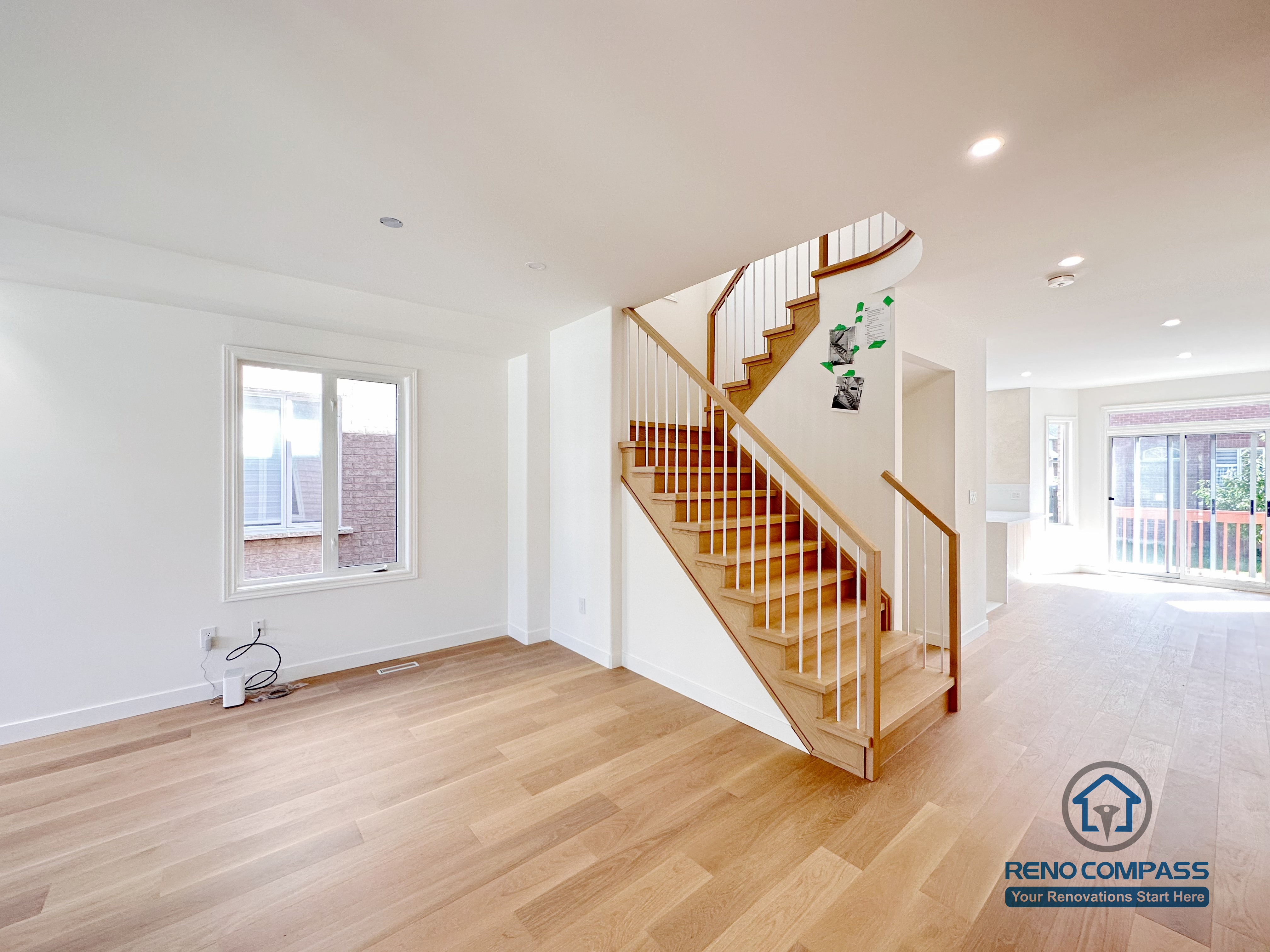 This image showcases a Markham flooring and stair renovation featuring wide-plank hardwood flooring and an open staircase with natural wood treads and white vertical railings. The seamless connection between the staircase and main living area enhances openness, light flow, and spatial continuity. Completed by a professional Toronto renovation company, Reno Compass Inc., the design balances modern simplicity with long-term durability.