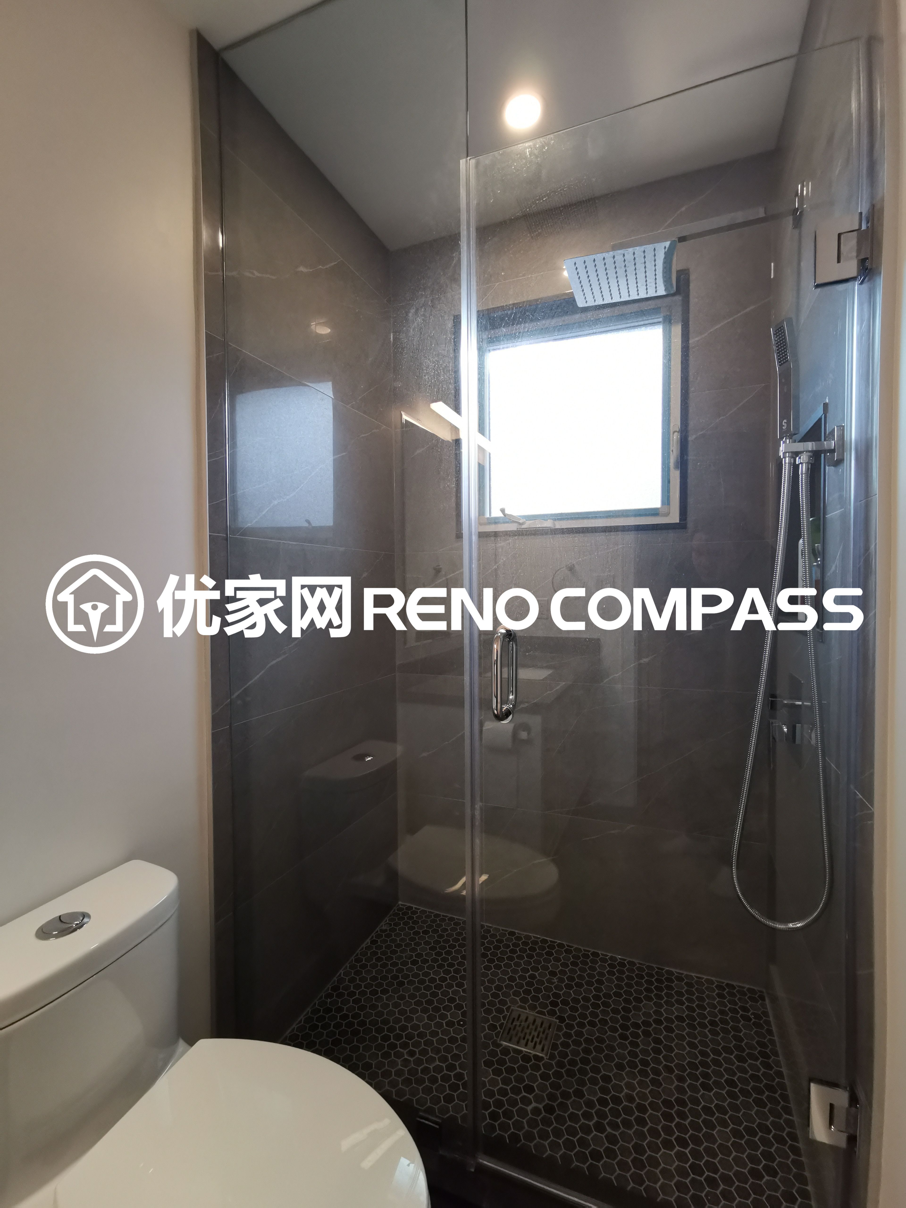 This image features a modern walk-in shower completed as part of a North York interior renovation project. The shower design includes a clear glass enclosure, large-format wall tiles, and a rain shower system that enhances both comfort and visual appeal. A mosaic tile shower floor provides slip resistance while adding subtle texture to the space. Natural light from the window improves brightness and ventilation, reflecting thoughtful bathroom planning and quality craftsmanship tailored for contemporary Toronto homes.