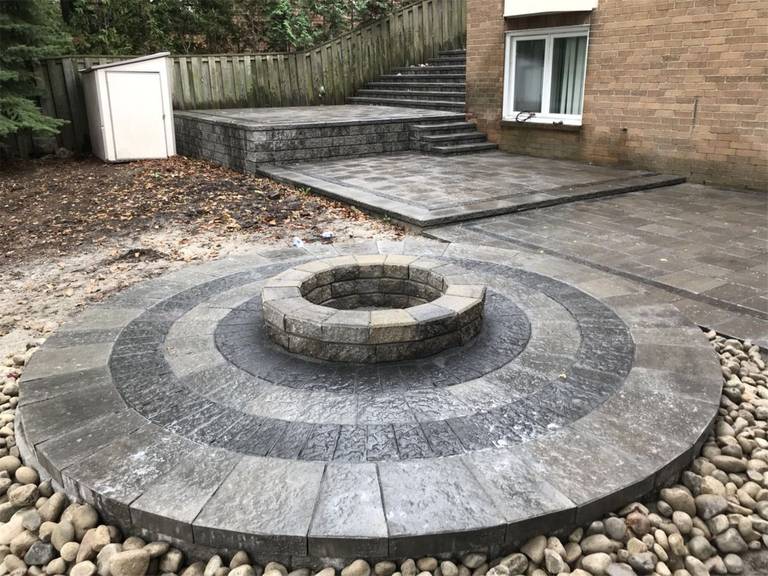 This Markham landscaping renovation features a custom circular fire pit surrounded by a beautifully designed interlocking stone patio. The layered stone pattern creates a striking focal point while providing a comfortable outdoor gathering space for family and guests. Completed by a trusted Toronto Renovation Company, the project enhances the backyard with durable materials, thoughtful design, and a warm outdoor entertainment area.