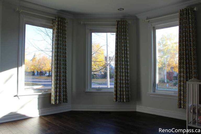 This Mississauga interior renovation project showcases a bright and elegant living space transformation featuring large bay windows, custom curtain installation, fresh neutral wall tones, and premium dark hardwood flooring. The upgraded space enhances natural lighting, improves comfort, and adds modern visual appeal, demonstrating the craftsmanship and detail-oriented work of a professional Toronto renovation company, Reno Compass Inc.