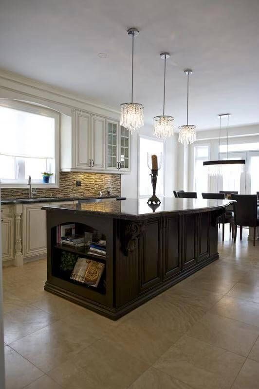 This European-inspired kitchen renovation features a large custom dark wood island with detailed paneling and built-in open shelving, creating both visual impact and functional storage. The contrasting white perimeter cabinetry enhances brightness while maintaining a timeless, classic aesthetic.

The island is topped with premium natural stone, offering ample workspace for cooking and entertaining. Elegant crystal pendant lights above the island add sophistication and warmth, complementing the neutral tile flooring and mosaic backsplash.

This kitchen layout emphasizes spaciousness, symmetry, and refined craftsmanship—ideal for homeowners seeking a high-end European kitchen renovation with a statement island centerpiece.