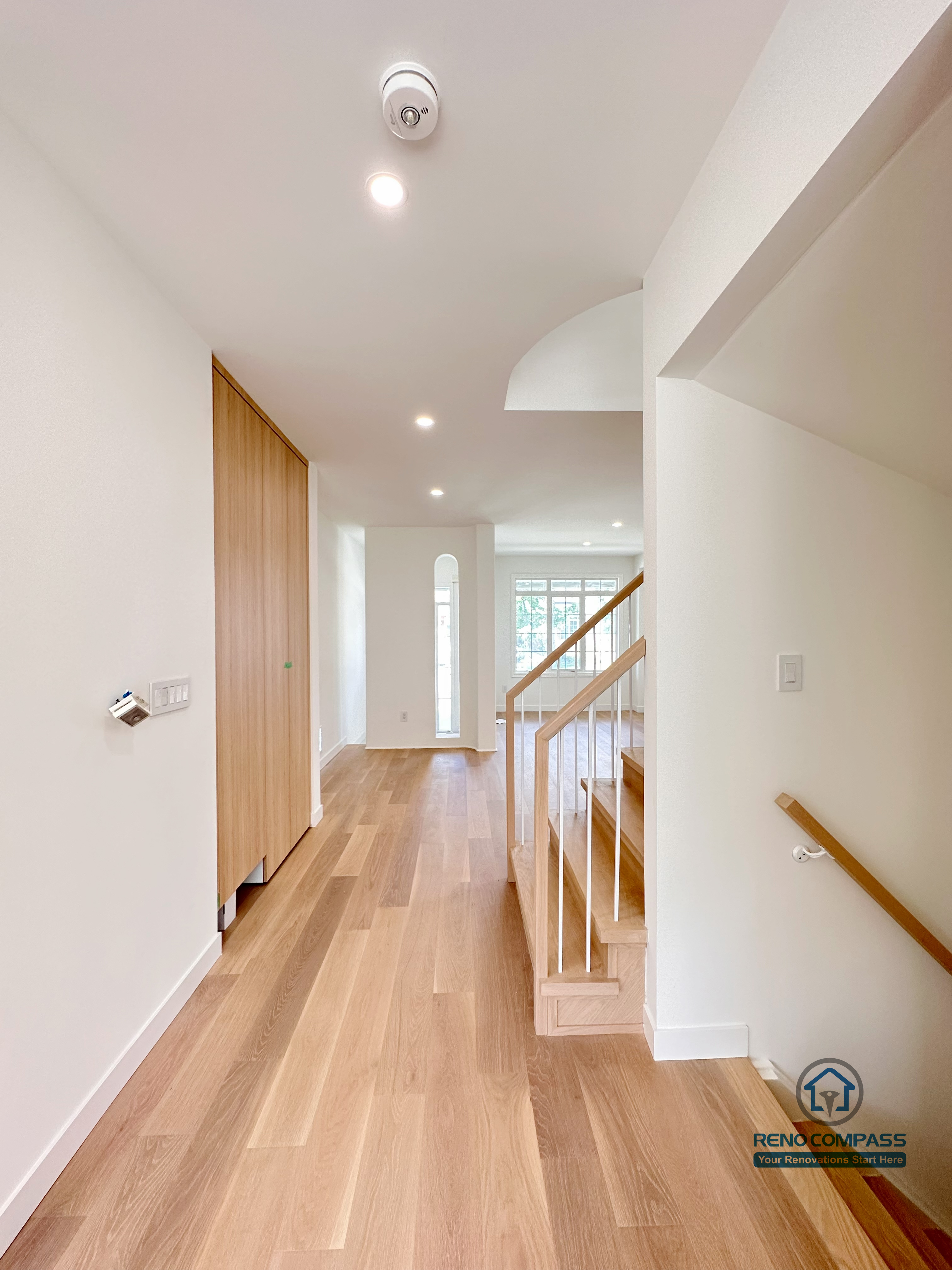 This image highlights a Markham flooring and stair renovation featuring continuous wide-plank hardwood flooring running through the hallway and seamlessly connecting to the staircase. Clean white walls, recessed lighting, and natural wood tones create a bright, minimalist circulation space with strong visual flow. Completed by a trusted Toronto renovation company, Reno Compass Inc., this design emphasizes durability, smooth transitions, and everyday functionality.