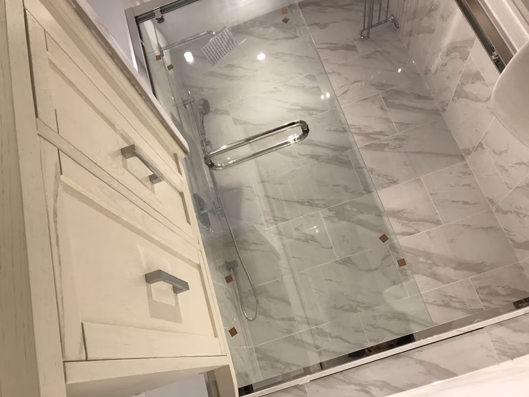 Elegant Toronto bathroom renovation featuring a frameless glass walk-in shower, marble-look wall tiles, brushed nickel fixtures, and custom vanity cabinetry for a luxurious, spa-inspired finish.