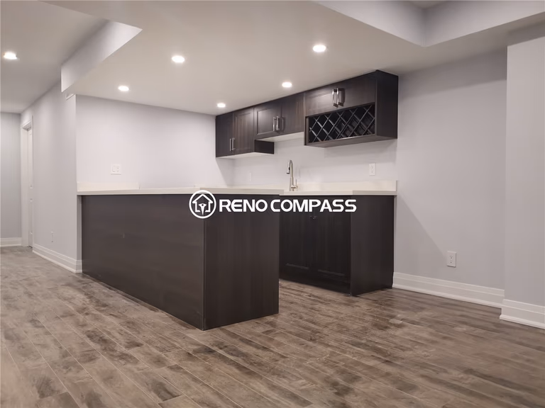 This Markham basement renovation features a custom-built bar and kitchenette area with dark wood cabinetry, integrated wine rack, modern sink, and a spacious countertop designed for entertaining and everyday convenience. Waterproof vinyl flooring and recessed pot lights enhance the modern basement atmosphere while ensuring durability and easy maintenance. The open layout creates a functional entertainment space perfect for gatherings or rental use. Completed by a professional Toronto renovation company, this project highlights quality millwork, precise installation, and practical basement remodeling tailored for homes across the Greater Toronto Area.