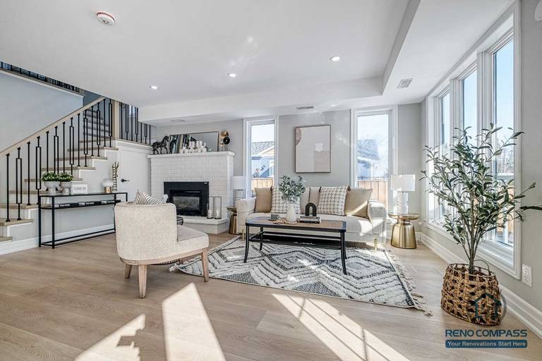This Georgian interior renovation features a bright living room with large windows, classic fireplace, elegant staircase railing, and light wood flooring. A refined and timeless interior completed by a professional Toronto renovation company.