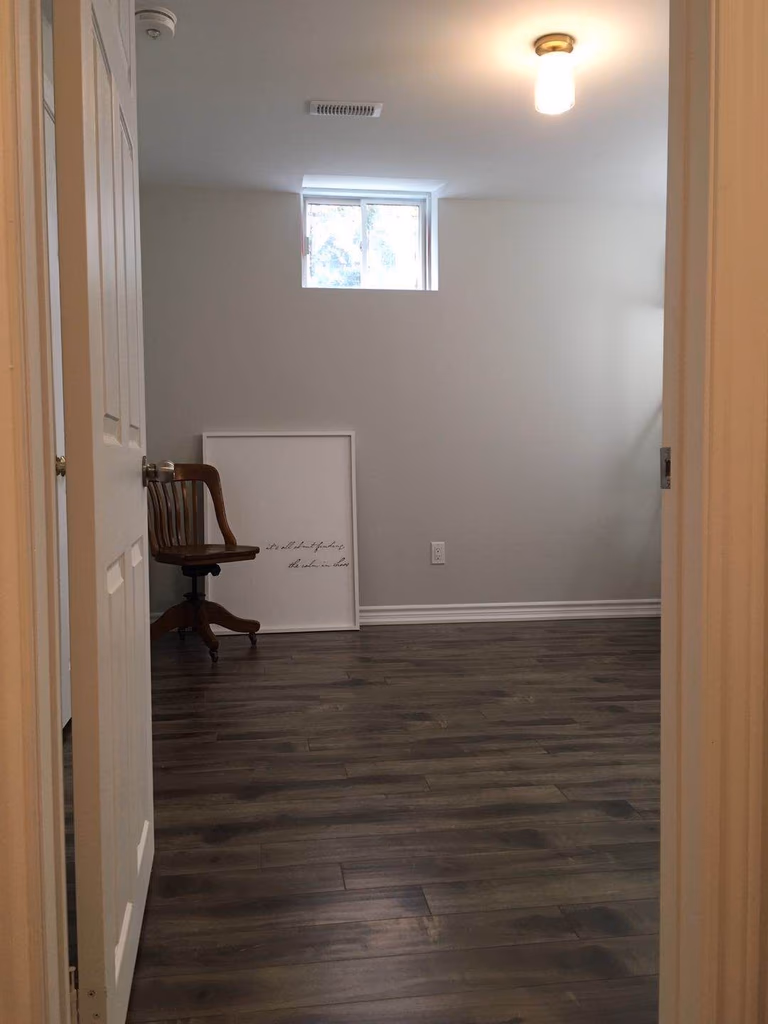 This Richmond Hill basement renovation showcases a clean and modern finished space with newly installed dark hardwood flooring, fresh neutral wall paint, upgraded ceiling lighting, and improved layout. The renovated basement room is designed to provide a comfortable and functional living or storage area, enhancing the home’s value and usability with a bright, contemporary finish.