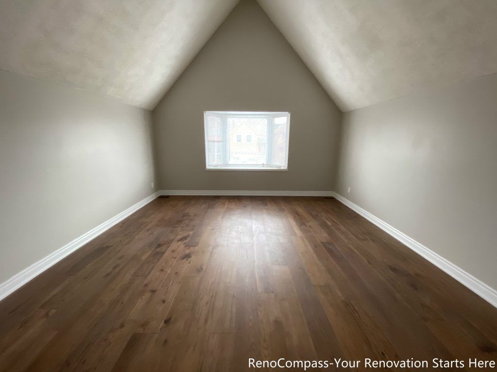 This Mississauga interior renovation features a bright attic bedroom with a sloped ceiling and wide-plank hardwood flooring. The symmetrical ceiling lines create a sense of height and openness, while the centered window allows natural light to evenly illuminate the space. Neutral wall colors and clean finishes enhance versatility, making this renovated attic room suitable for use as a bedroom, office, or multi-purpose living area.