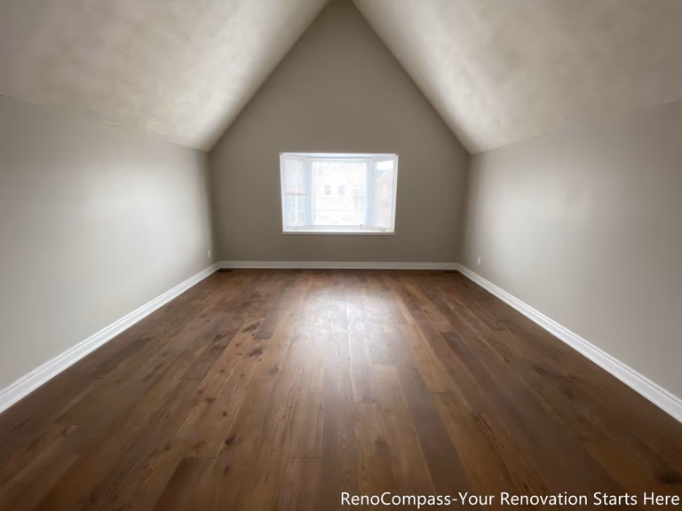 This Mississauga interior renovation features a bright attic bedroom with a sloped ceiling and wide-plank hardwood flooring. The symmetrical ceiling lines create a sense of height and openness, while the centered window allows natural light to evenly illuminate the space. Neutral wall colors and clean finishes enhance versatility, making this renovated attic room suitable for use as a bedroom, office, or multi-purpose living area.