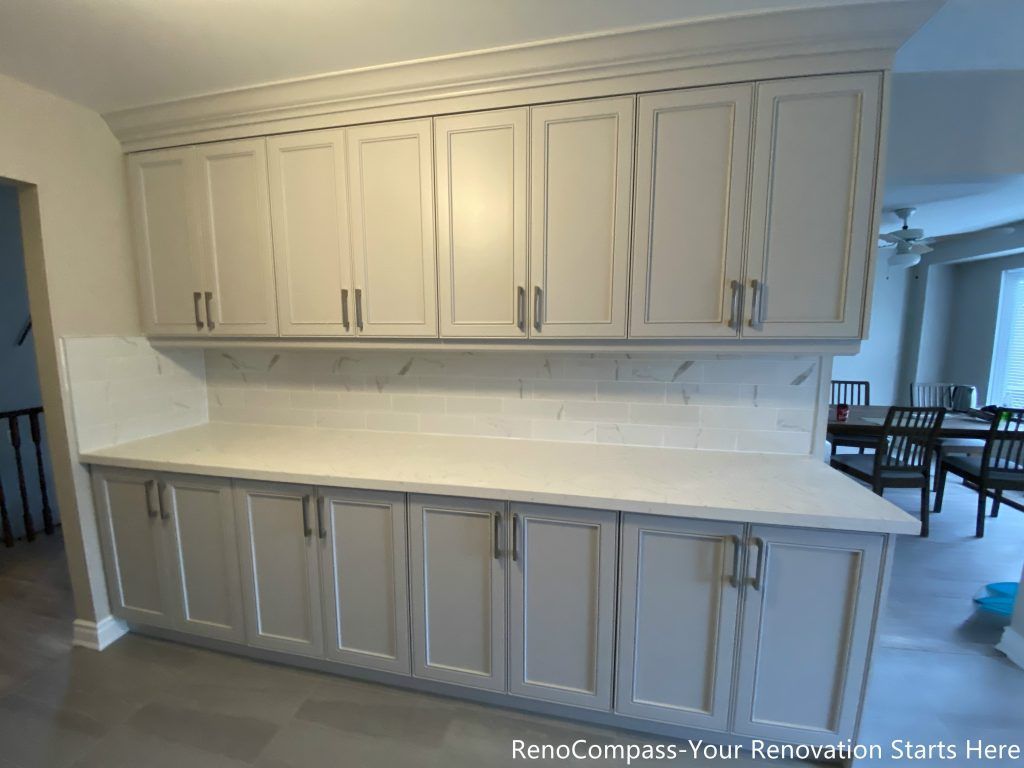 This Mississauga interior renovation features a full-height custom kitchen storage wall with soft gray shaker cabinets and a seamless quartz countertop. The extended cabinetry design maximizes storage capacity while maintaining a clean, balanced visual rhythm. Integrated crown molding and minimalist hardware enhance the overall kitchen renovation, creating a practical and elegant storage solution for everyday family use.