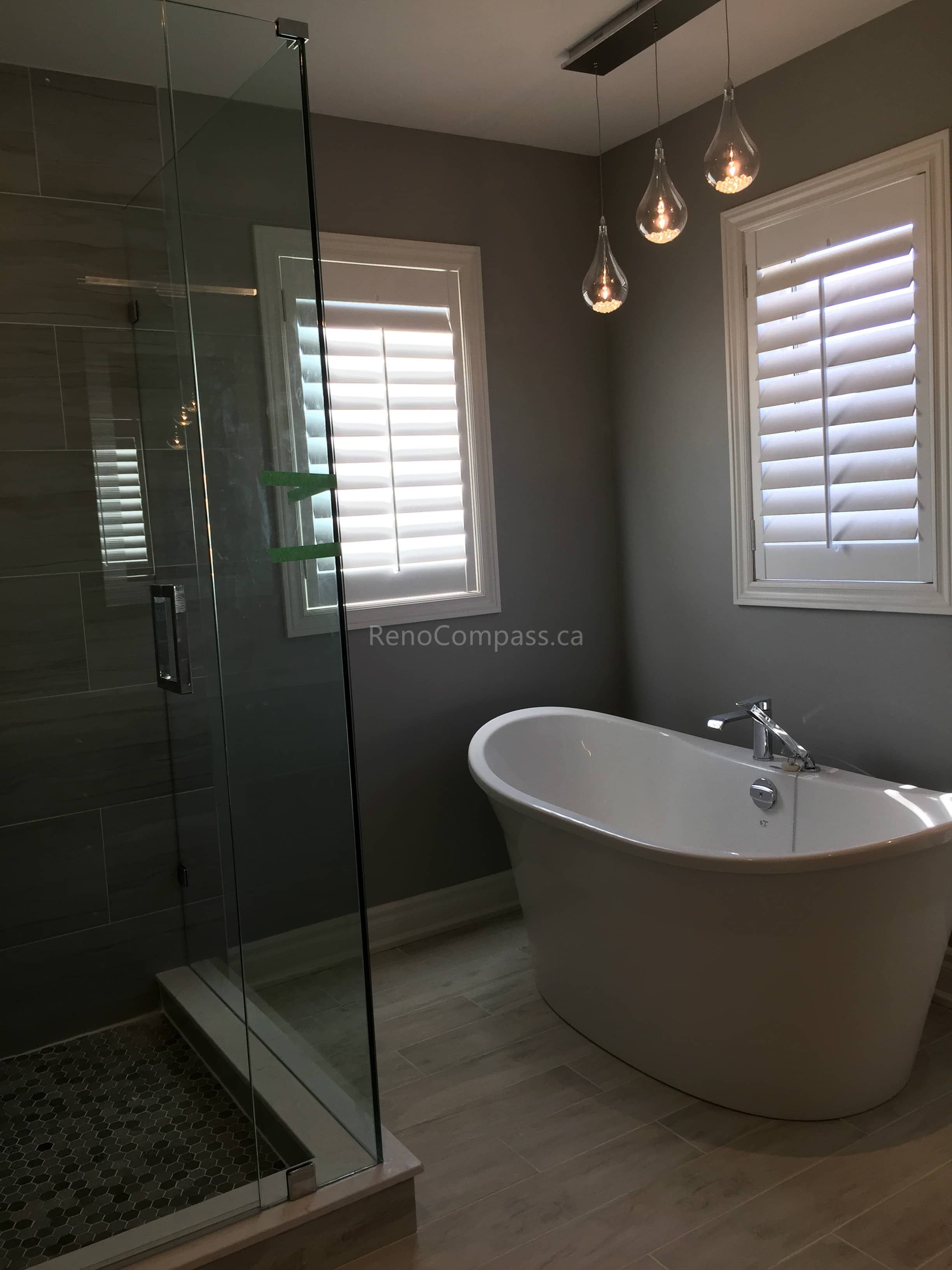 A spa-inspired bathroom interior renovation in Toronto featuring a glass-enclosed walk-in shower, freestanding bathtub, modern pendant lighting, and neutral-toned finishes. The space balances functionality and relaxation, showcasing refined Toronto interior renovation and interior design craftsmanship.