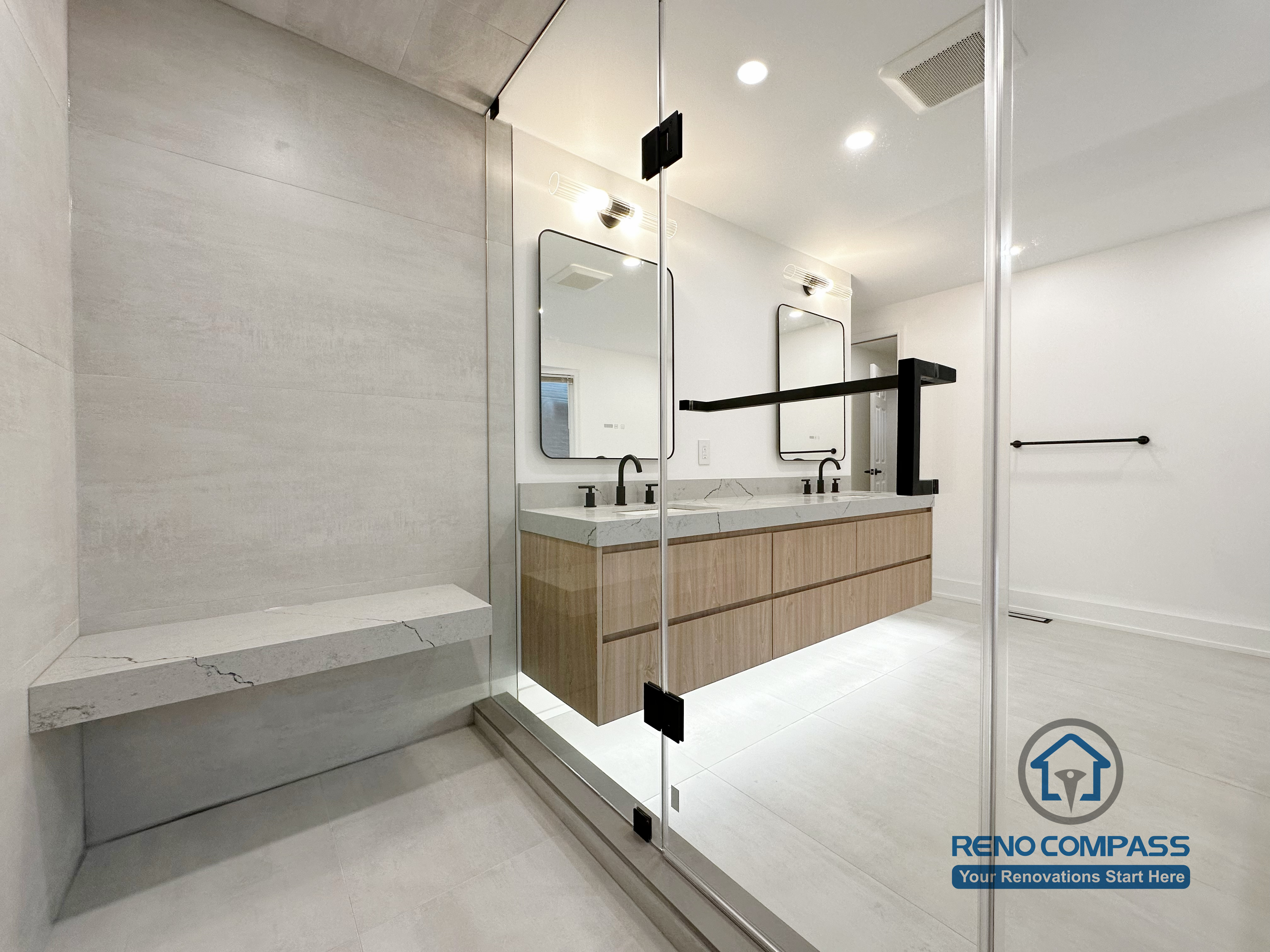 Modern bathroom renovation in Oakville featuring a frameless glass shower, built-in shower bench, and custom double vanity with quartz countertop, completed by a professional Toronto renovation company.