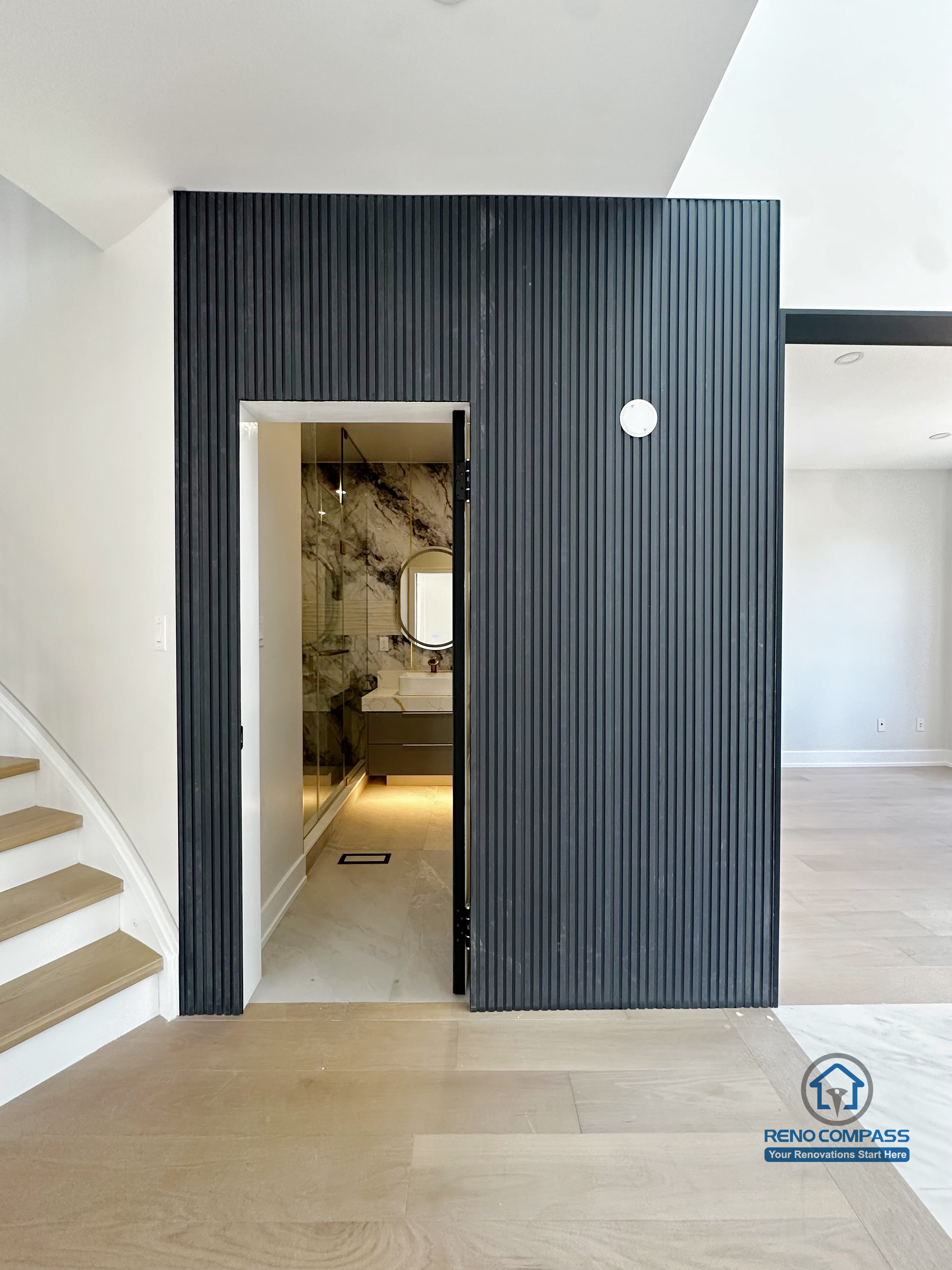 This Markham interior renovation highlights a bold vertical slat feature wall that defines circulation while adding architectural depth to the space. The recessed powder room entrance is seamlessly integrated into the wall, creating a clean and intentional transition between public and private areas. Natural wood flooring, soft neutral tones, and carefully planned lighting work together to enhance spatial clarity and visual balance. The result is a modern interior that feels structured, refined, and thoughtfully detailed.