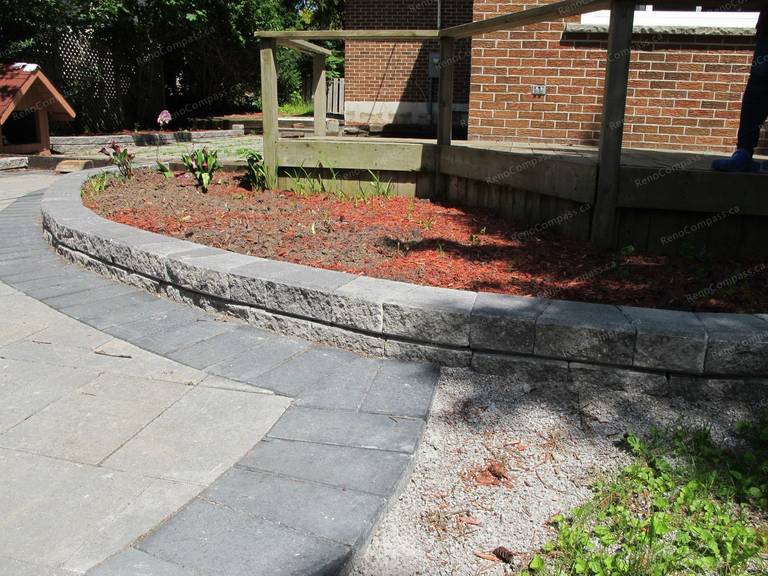 This Markham landscaping project showcases a custom-built garden bed constructed with durable interlock stone. The curved interlock edging creates a clean and structured flower bed layout while enhancing the overall backyard design. Filled with fresh mulch and ready for planting, the raised flower bed adds depth and visual interest to the outdoor space. Completed by Reno Compass Inc., this project highlights professional craftsmanship in interlock landscaping and garden design, delivering a low-maintenance and elegant outdoor environment for homeowners.
