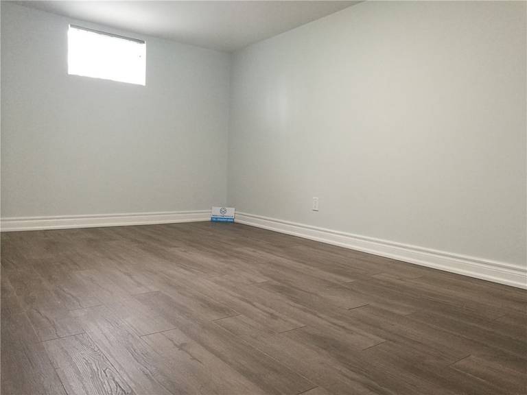Finished interior space from a Pickering basement renovation project featuring new wood-look flooring, clean white walls, baseboard trim, and a bright window for natural light. This simple and functional room upgrade improves comfort and usability, completed by a professional Toronto renovation company.